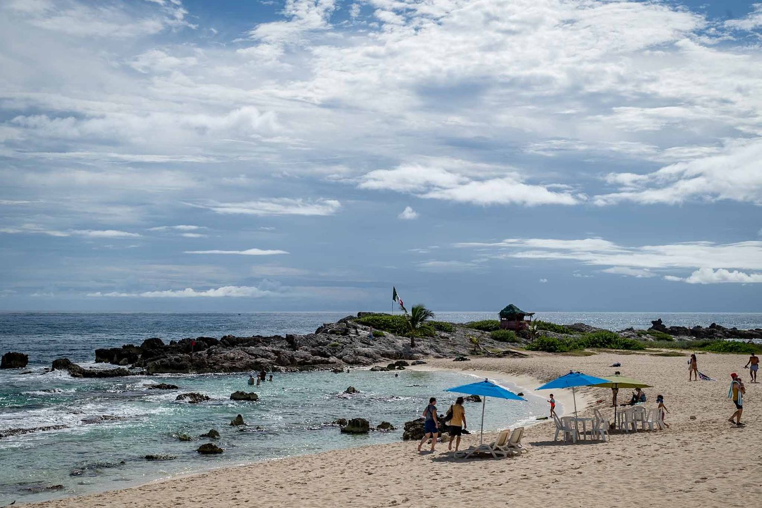Rocky beach cove with blue umbrellas and chairs overlooking the ocean on a sunny day.