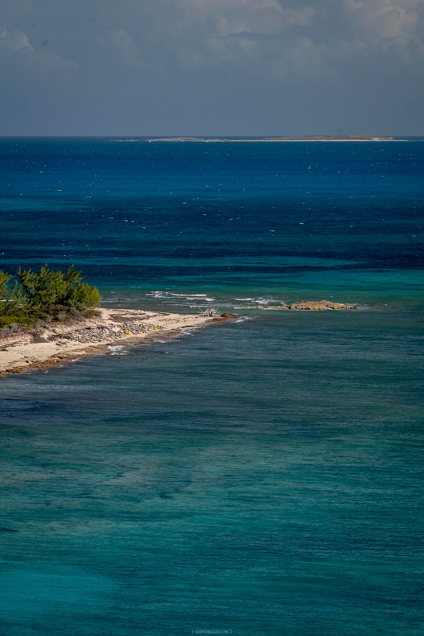 Turquoise Caribbean waters meet a sandy shoreline with lush greenery, with a distant island visible on the horizon.