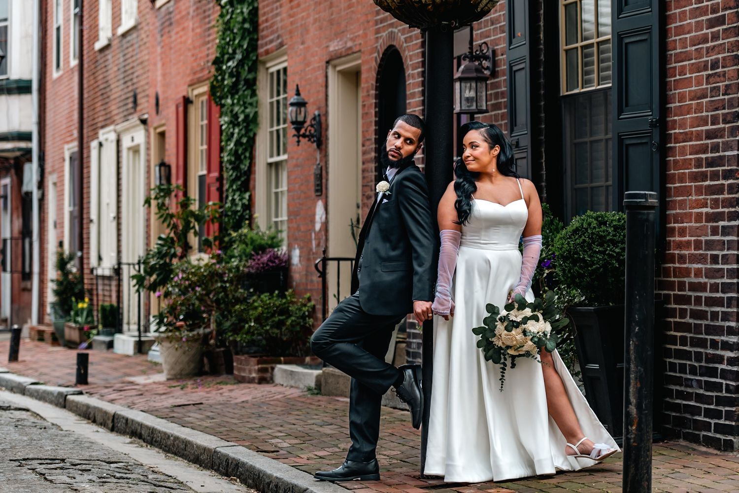 Elegant bride and groom posing on a historic cobblestone street lined with brick buildings on their wedding day.