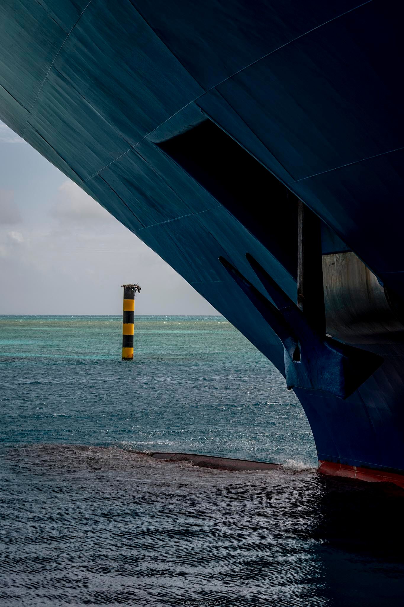 View of yellow and black striped nautical marker through the hull of a large blue cruise ship.