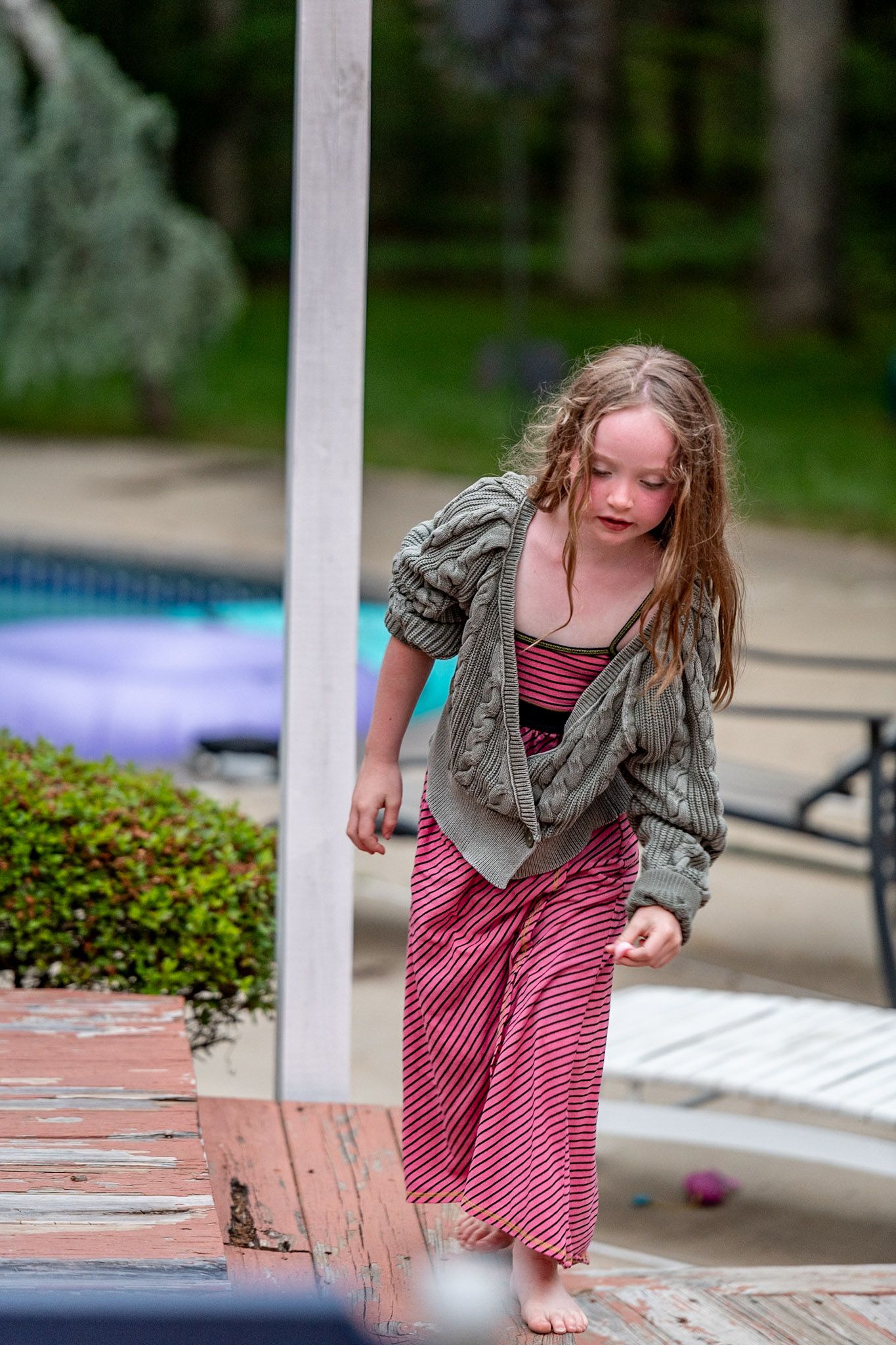 Someone in a striped dress and gray jacket moving playfully outdoors.