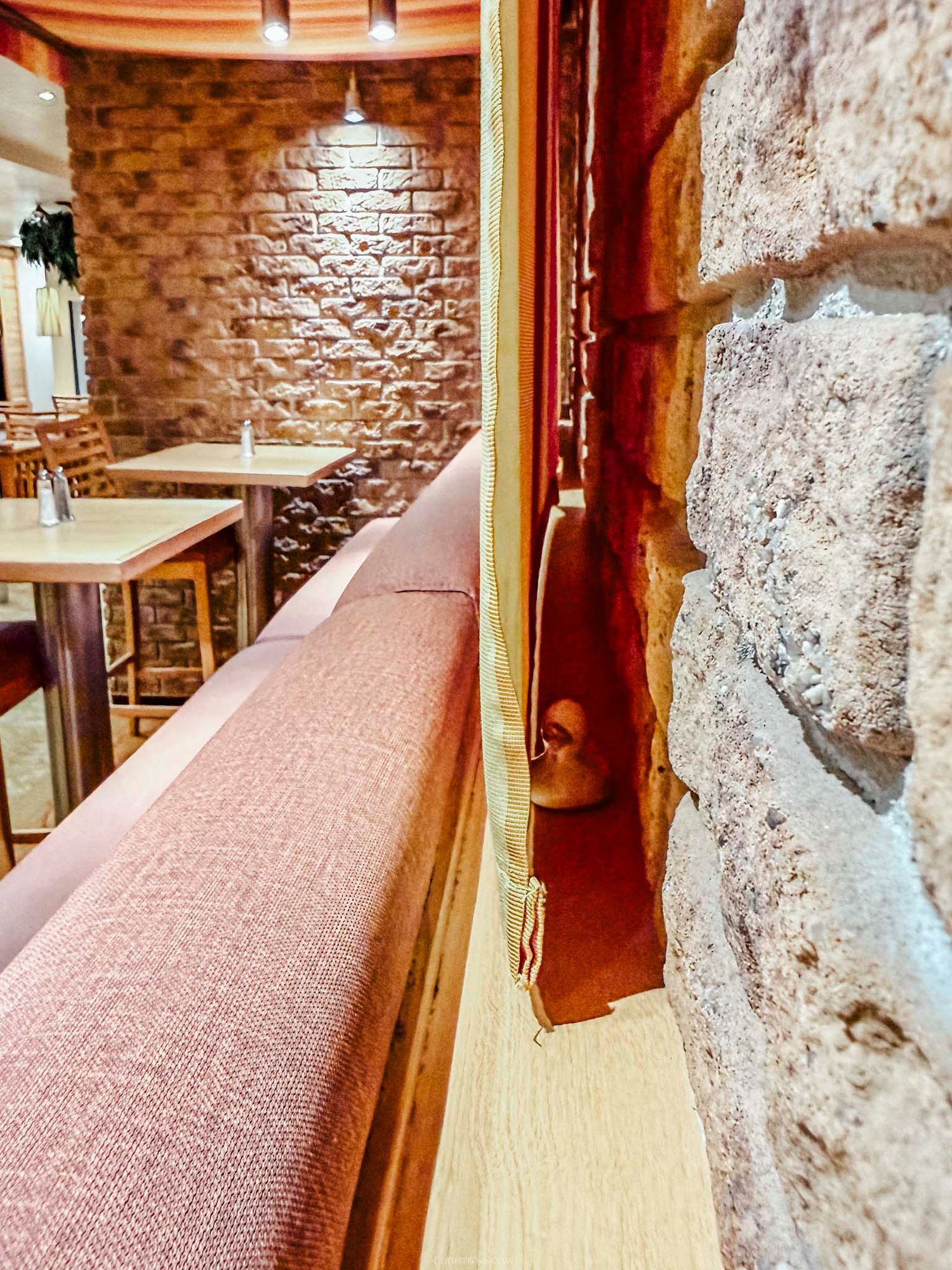 Close-up of a rustic stone wall beside a pink upholstered bench seat in a cozy restaurant interior.