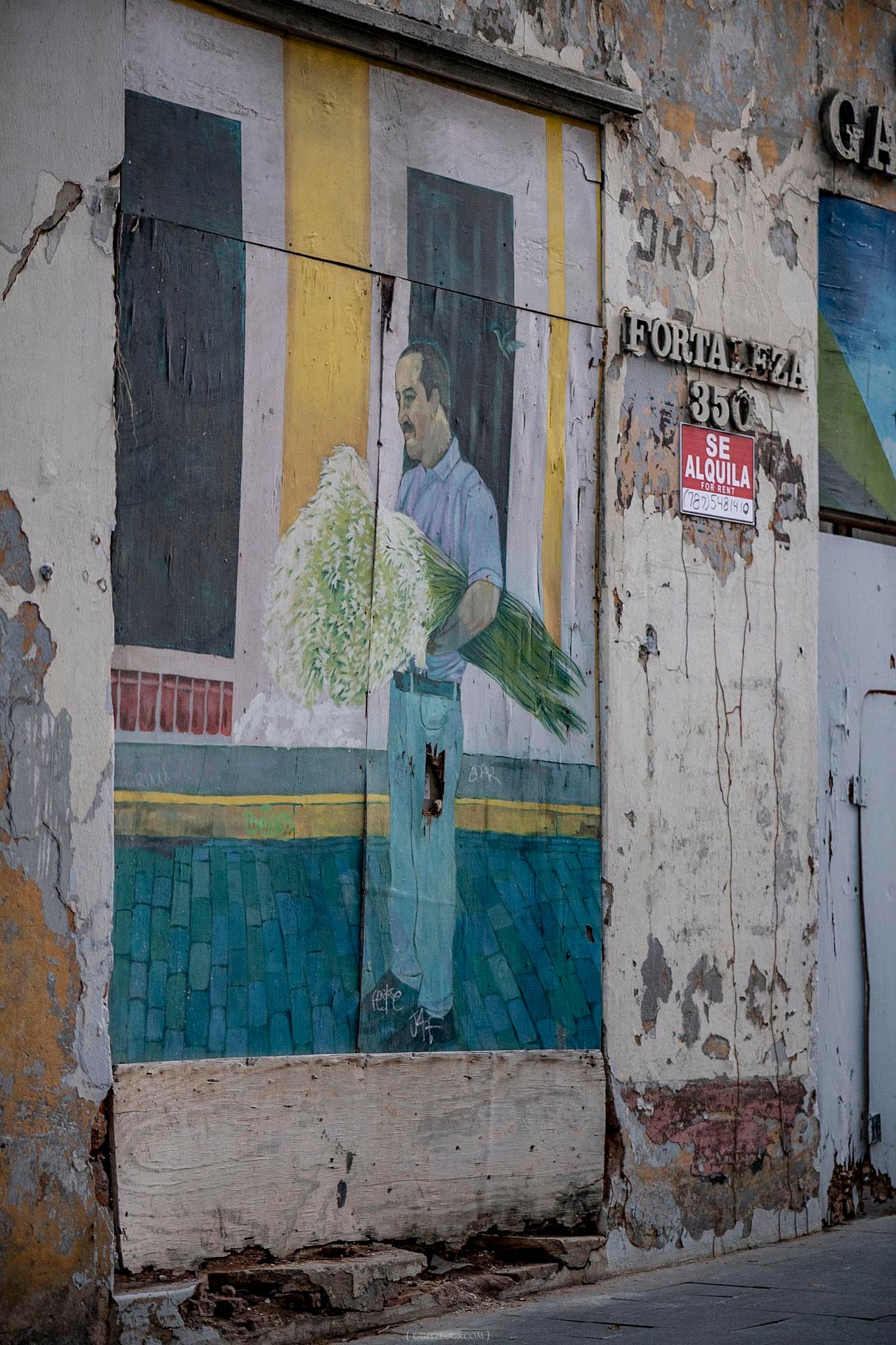 Street mural on weathered wall showing man holding green plants, with 'Se Alquila' sign, Fortaleza 350.