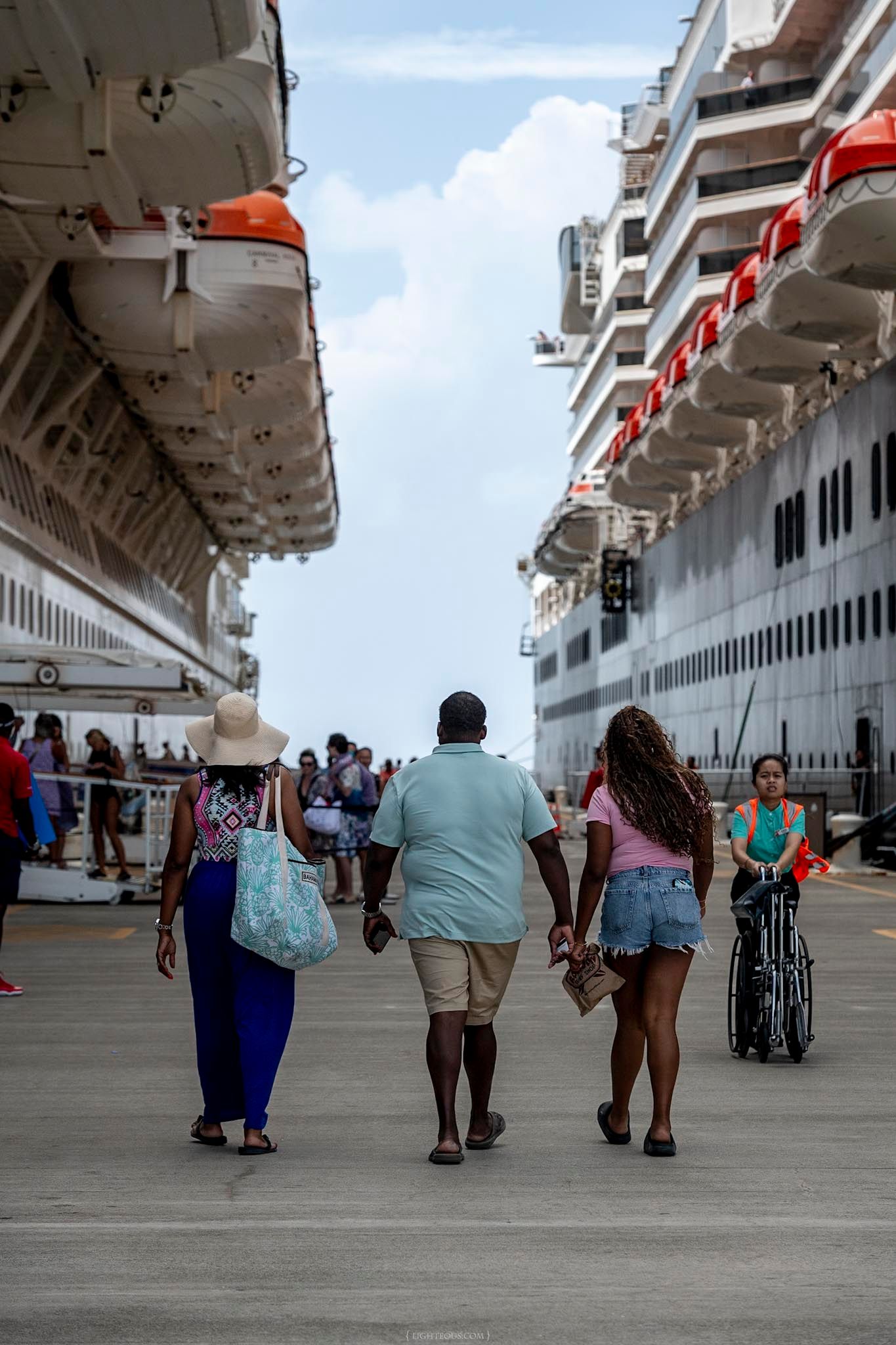 Tourists walking between two large cruise ships docked at a sunny Caribbean port terminal.