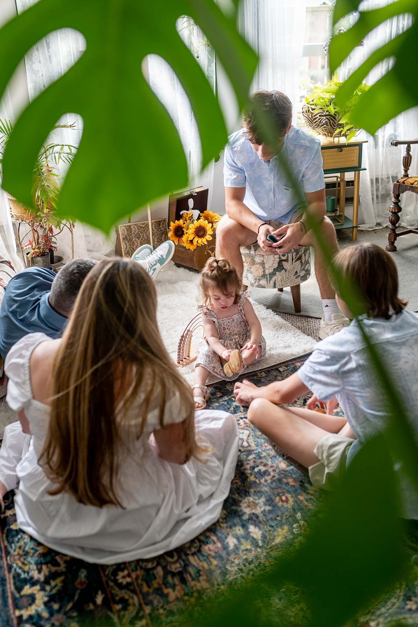 Indoor scene with houseplants framing a patterned rug and white furniture.