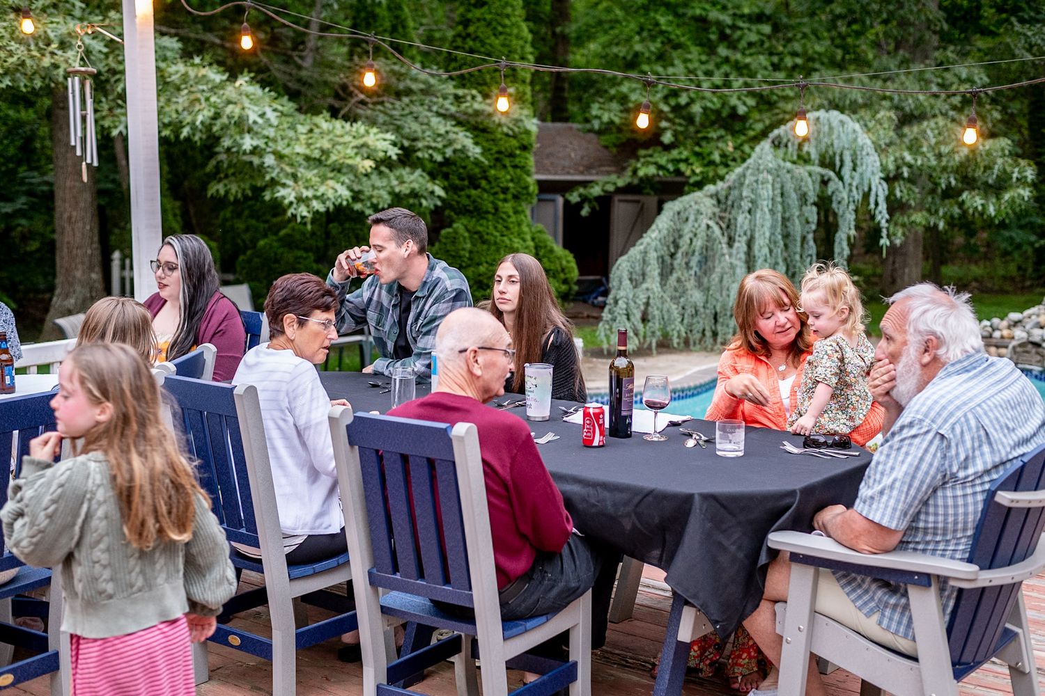 People enjoying conversation at outdoor tables during a backyard party with decorative lighting.