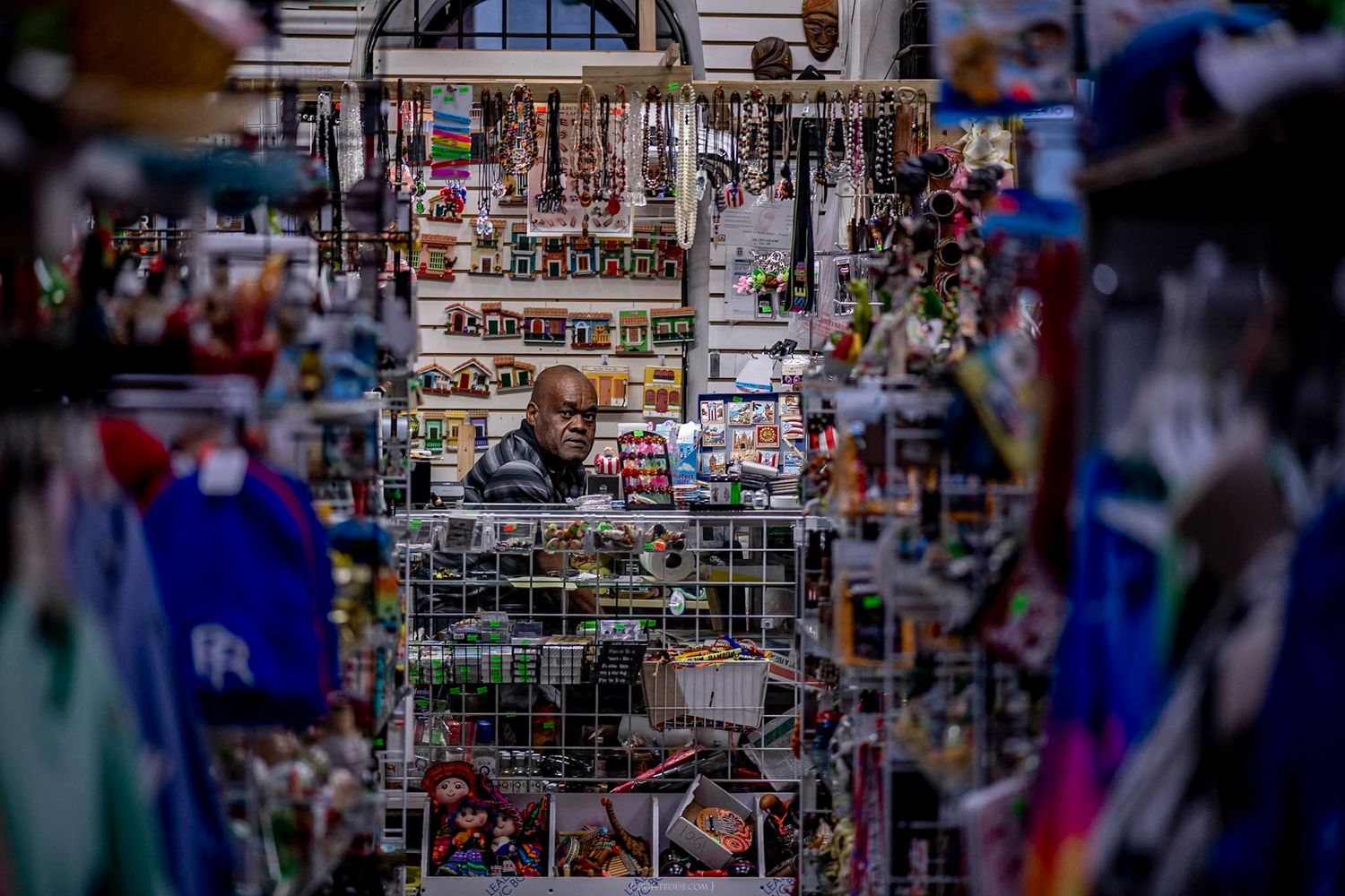 A vendor surrounded by colorful souvenirs and merchandise at a busy tourist market stall.