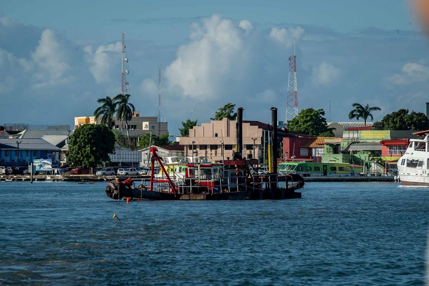 Panoramic waterfront view of coastal buildings and docks with palm trees under blue sky.