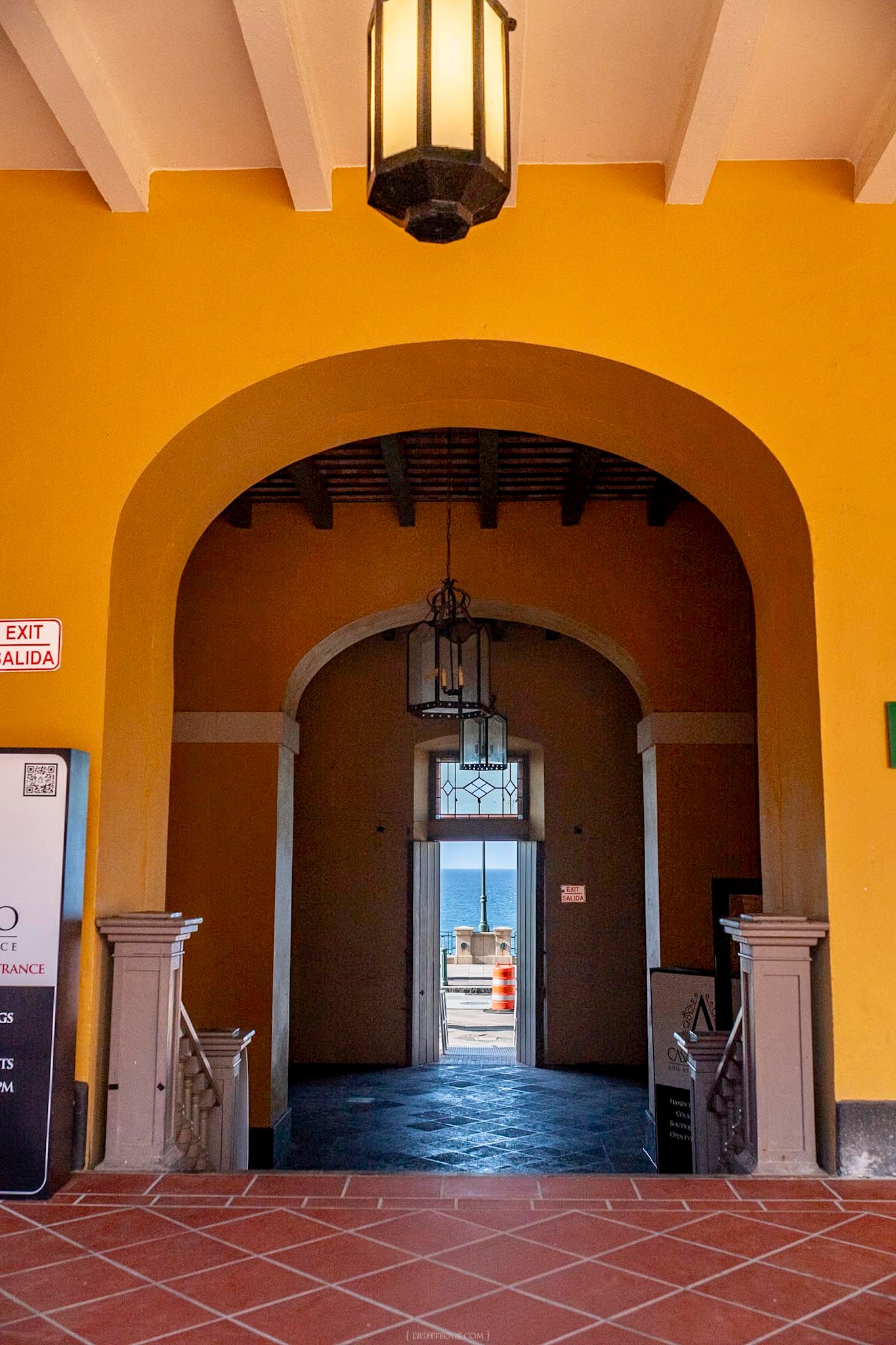 Yellow archway entrance with hanging lanterns leading to ocean view, colonial architecture with terracotta tile floors.