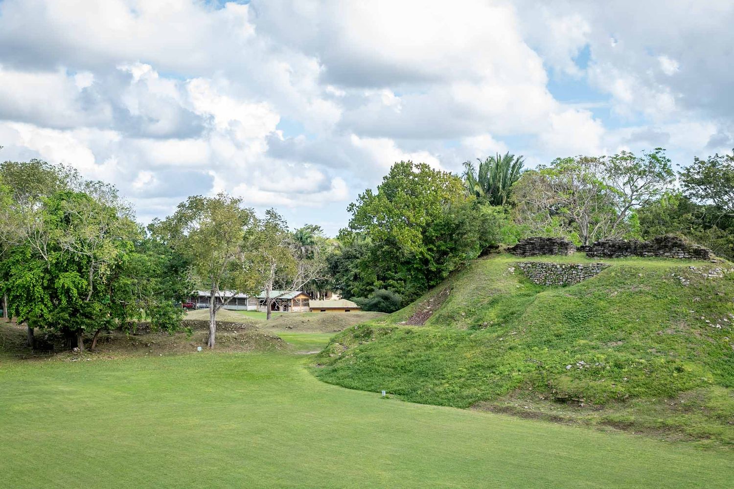 Wide landscape view of grassy hills and vegetation under a cloudy blue sky.