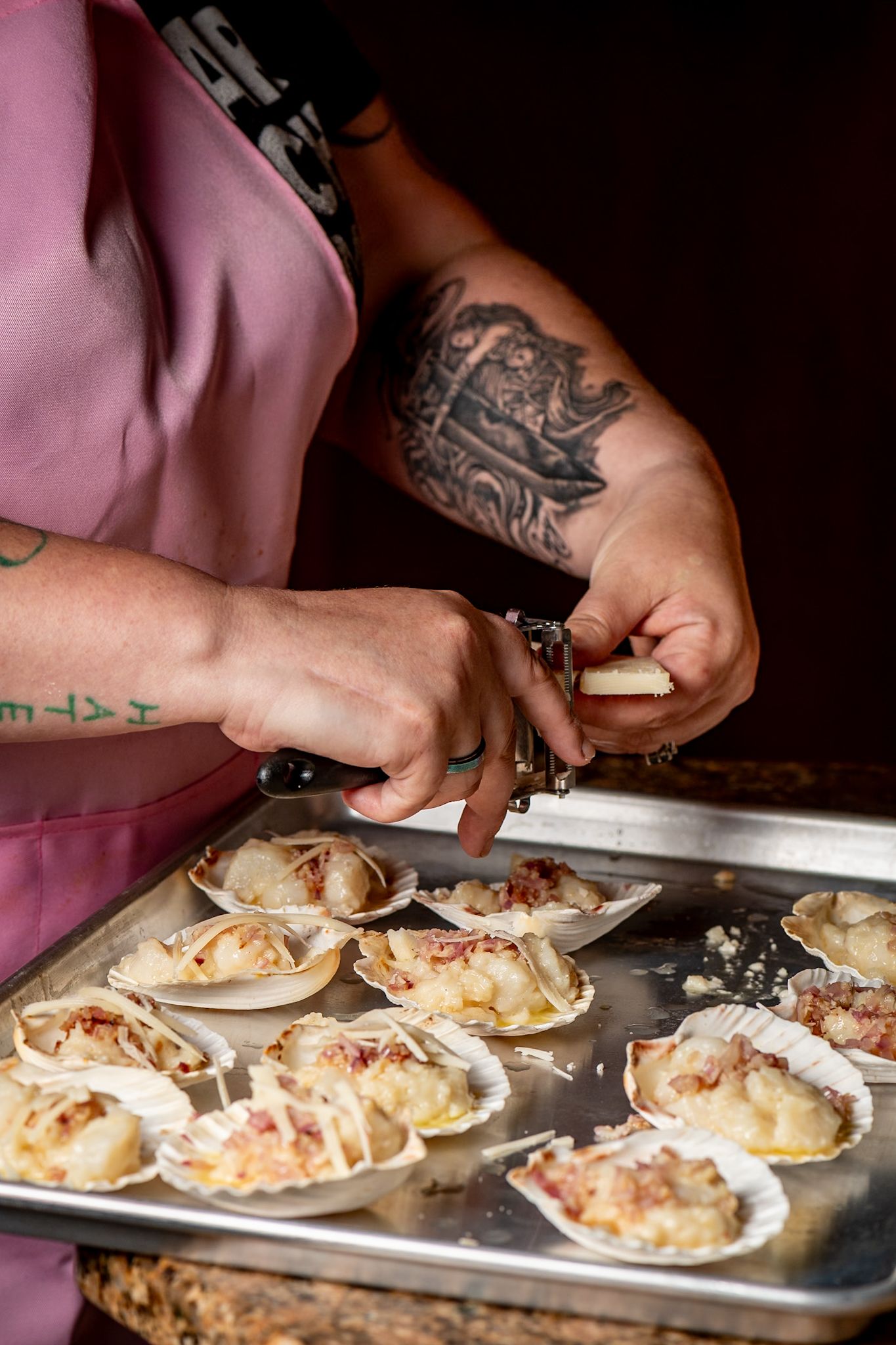 Chef preparing seafood appetizers on metal tray with detailed arm tattoo visible.