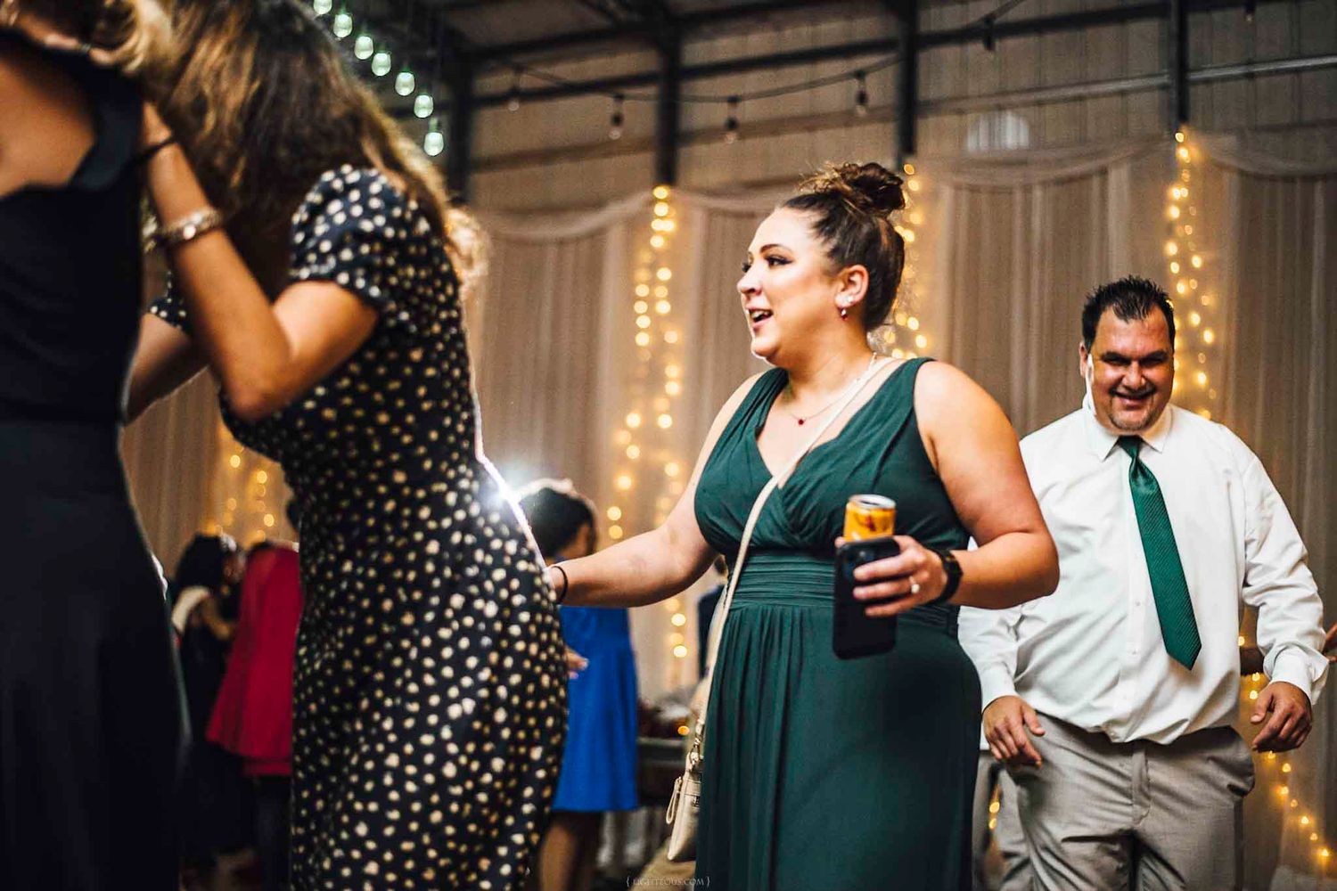 Woman in green dress dancing and smiling at a wedding reception with string lights in background.