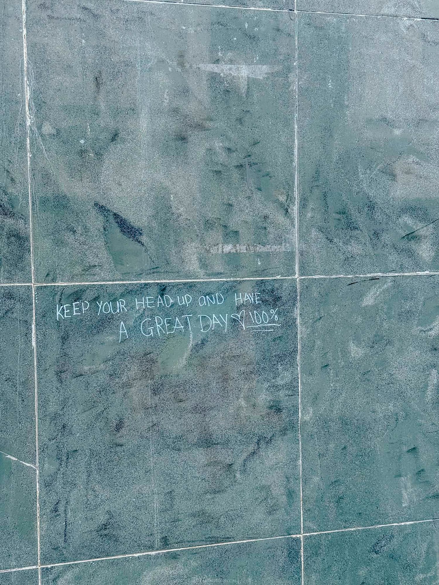 Green marble wall tiles with inspirational graffiti message reading Keep Your Head Up and Have a Great Day.