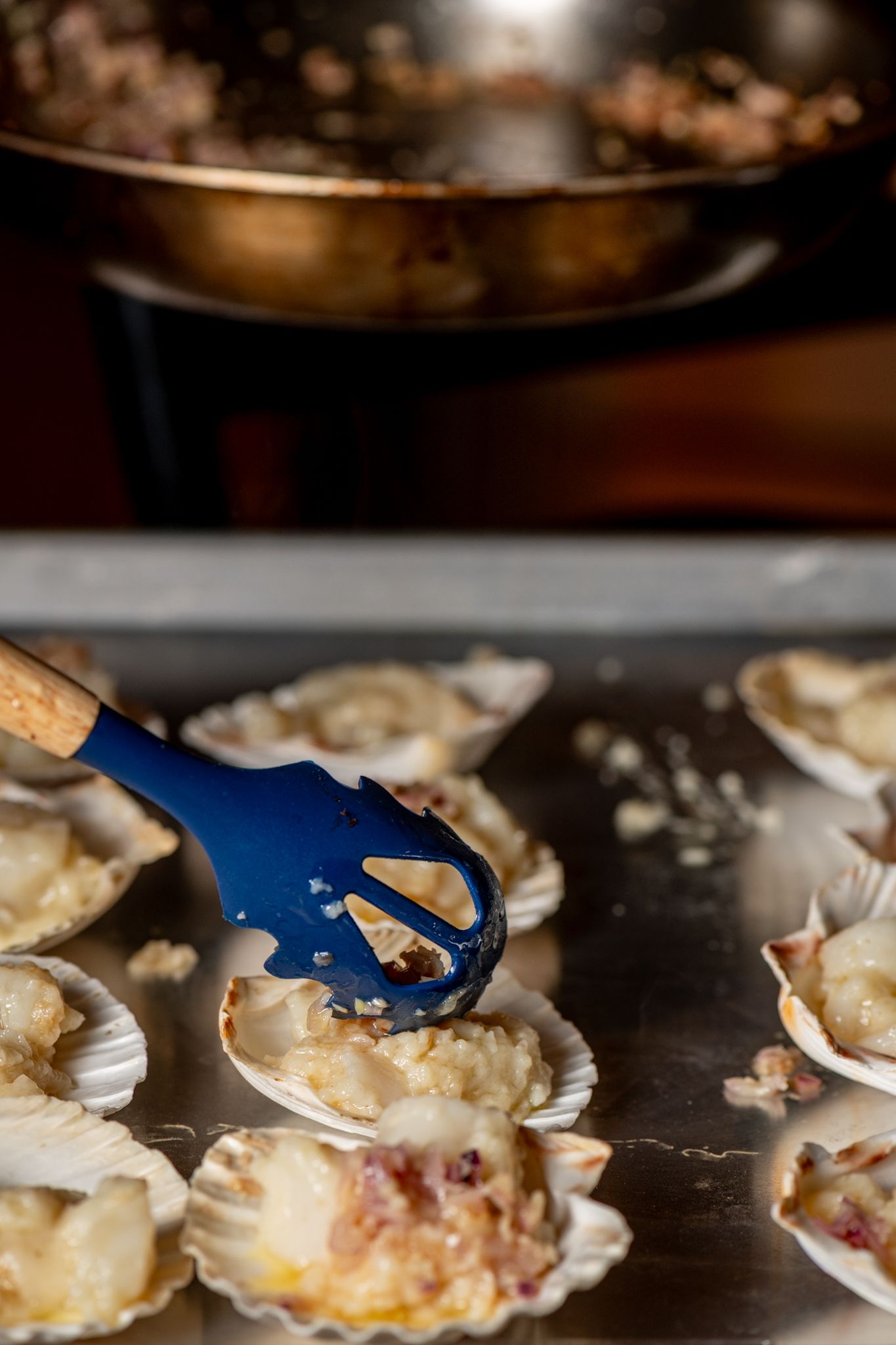 Close-up of scallops being prepared on a dark surface with blue utensils.
