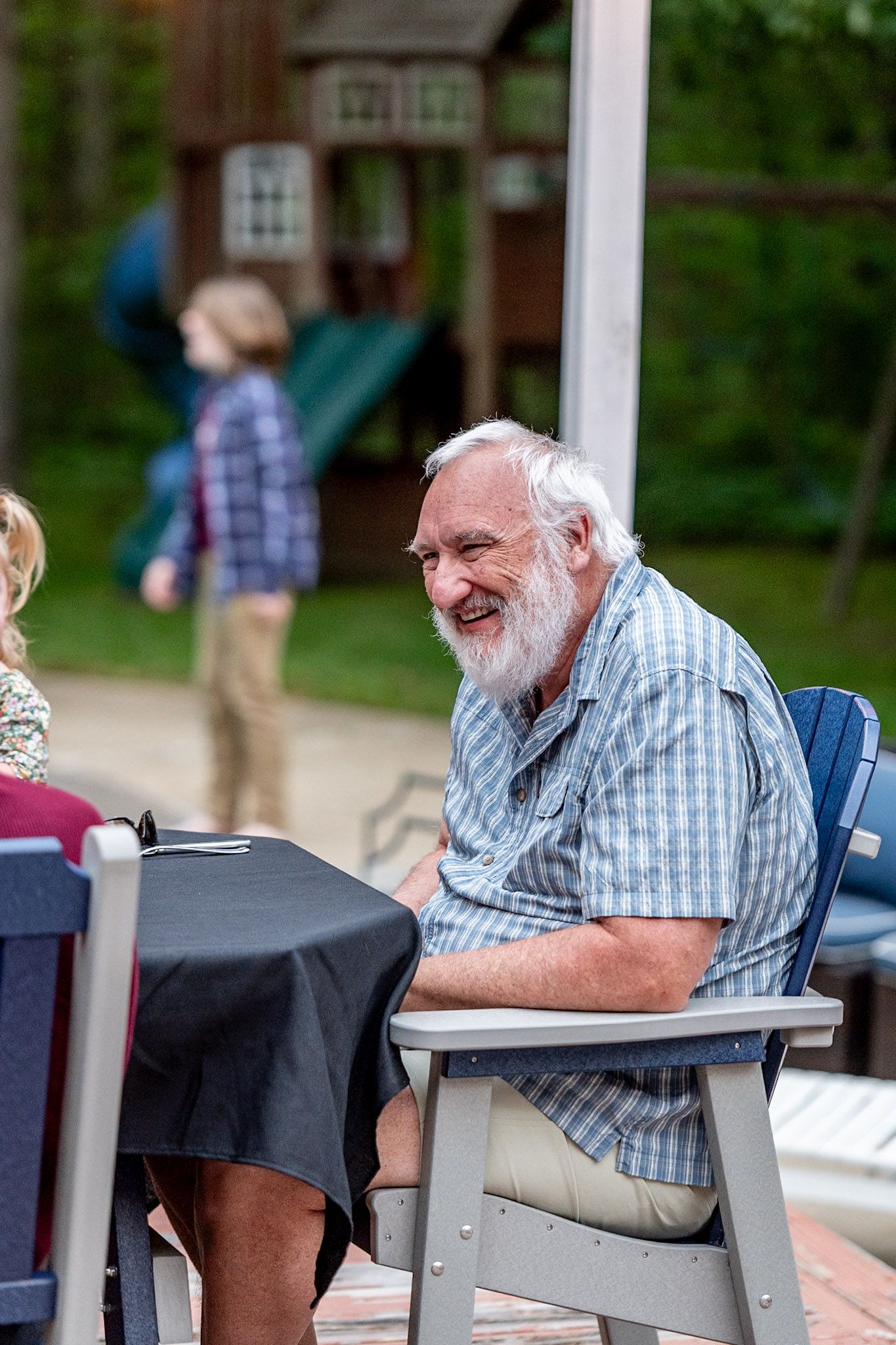 Someone laughing heartily while seated at an outdoor table during a social gathering.