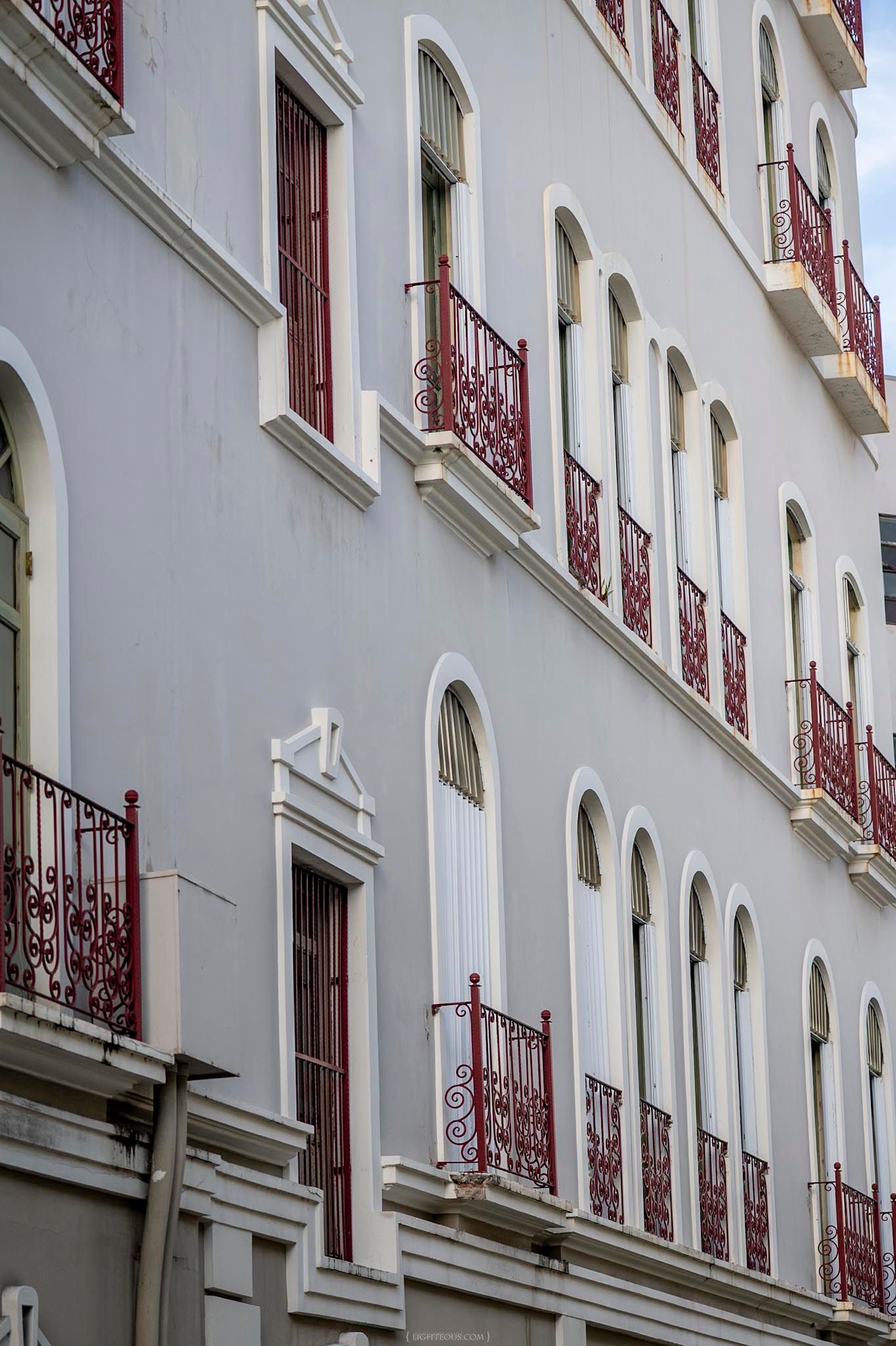 White colonial building facade with ornate red iron balconies and arched windows.