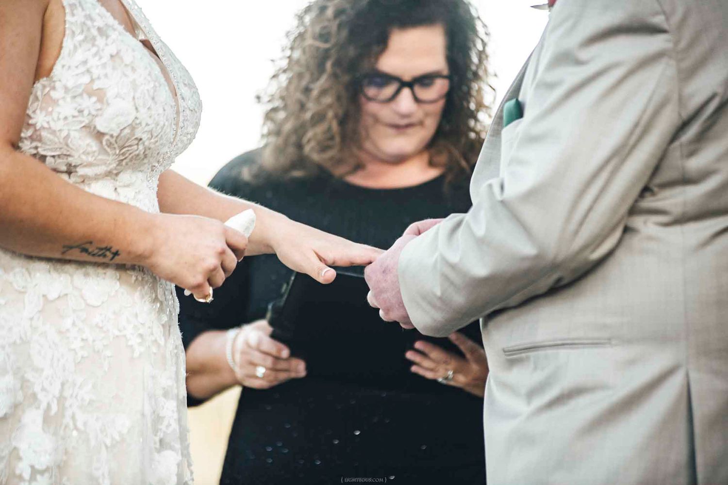 Wedding officiant places ring on bride's finger during an intimate outdoor ring exchange ceremony.