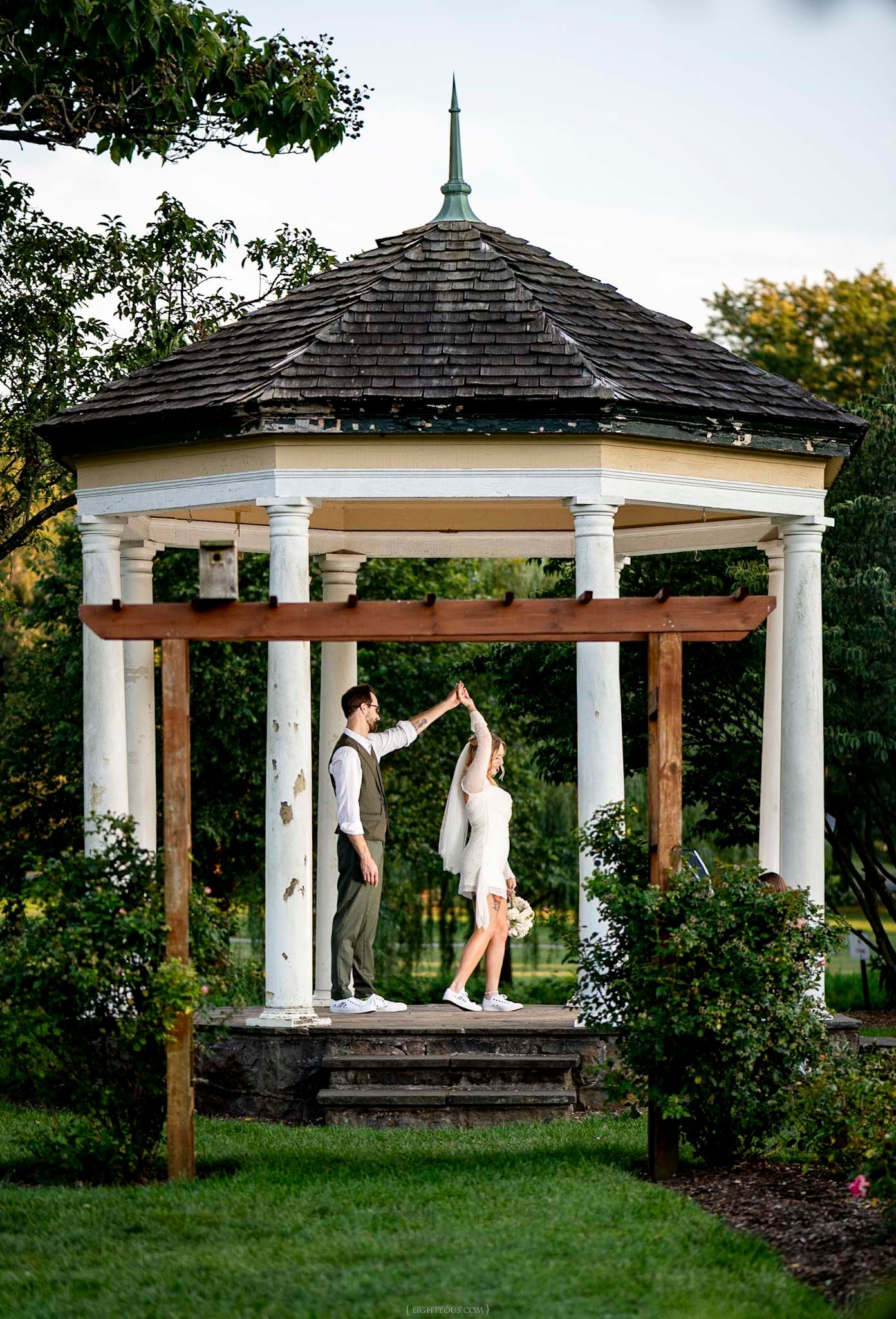 Couple dancing under a white gazebo surrounded by lush greenery during an outdoor wedding celebration.
