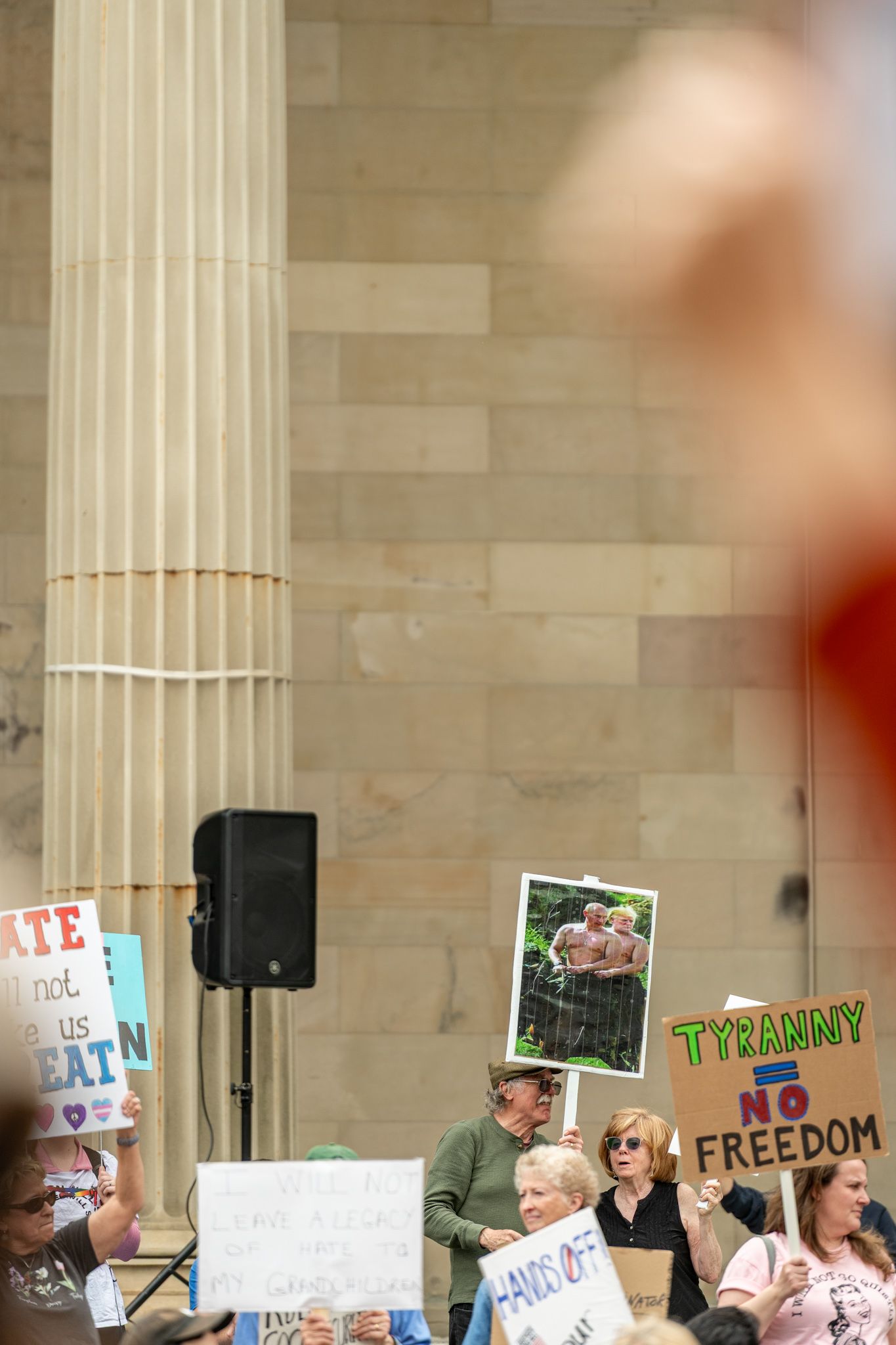 Protesters gathered in front of a building with classical columns holding signs about freedom and tyranny.