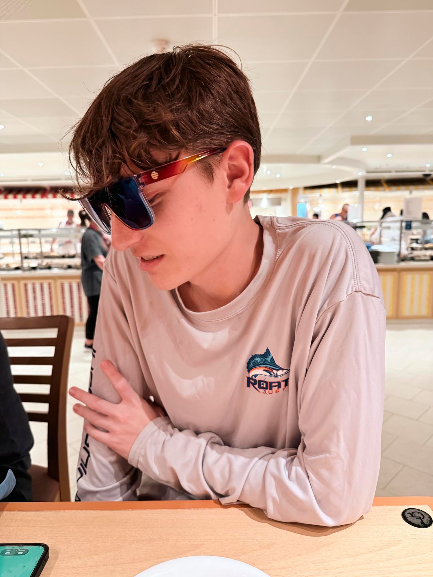 Young man wearing sunglasses and a beige long-sleeve fishing shirt sitting at a restaurant table.