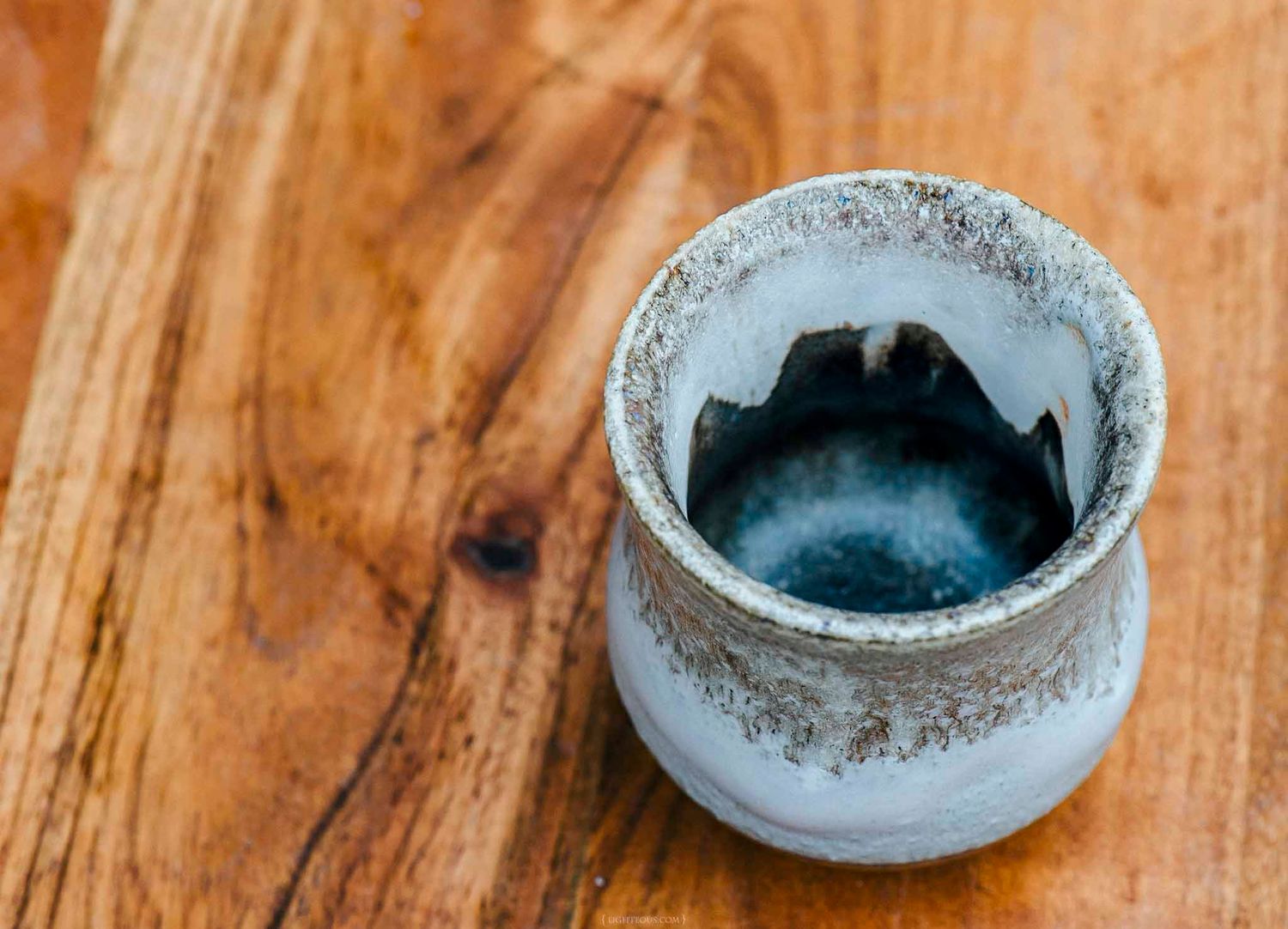 Rustic ceramic sake cup with blue glaze interior on wooden table.