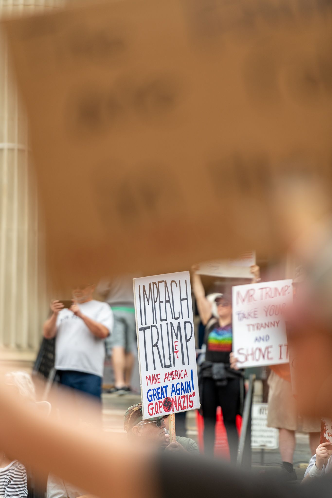 Crowd holds protest signs high in the air against a backdrop of institutional architecture.