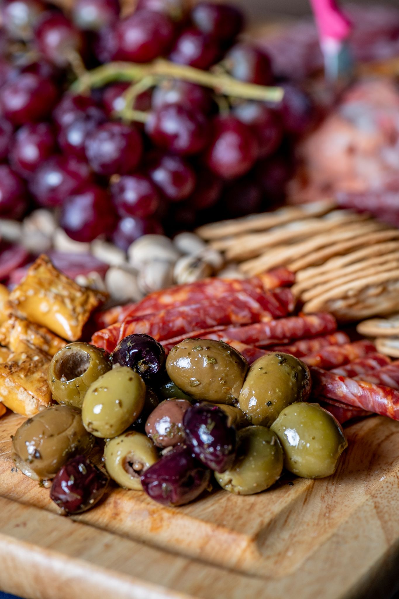 Charcuterie board with olives, grapes, and cured meats arranged on wooden serving platter.