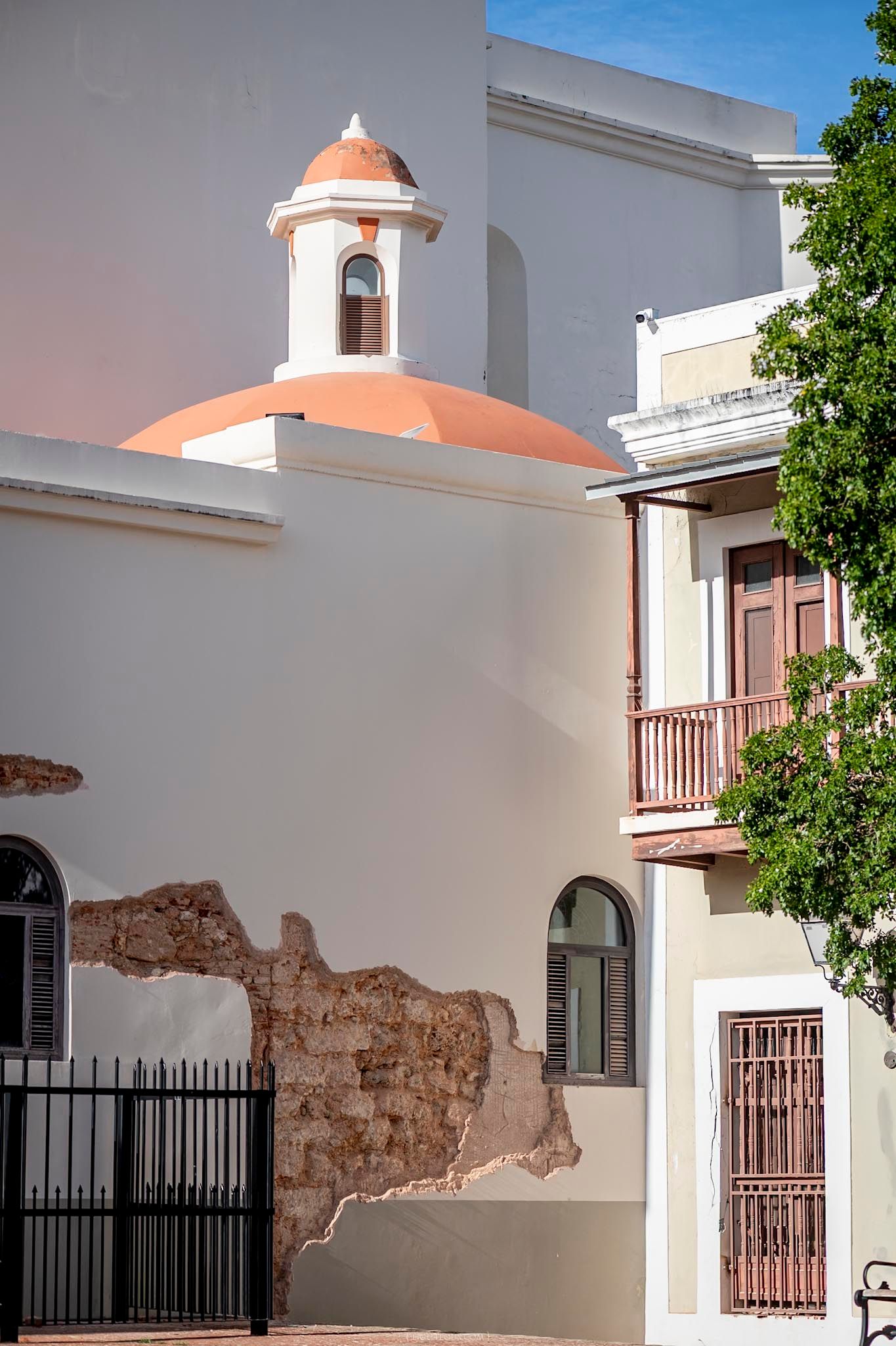 Historic white colonial building with terracotta dome bell tower and exposed brick wall in Old San Juan.