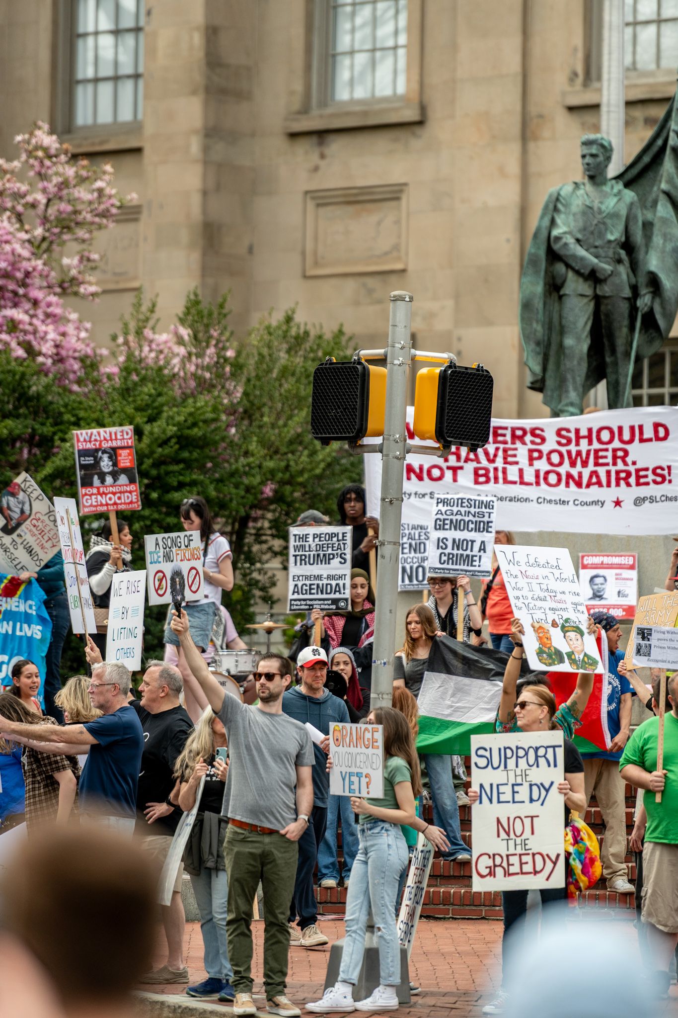 Demonstrators gather outside a stone building holding signs about economic inequality and power.