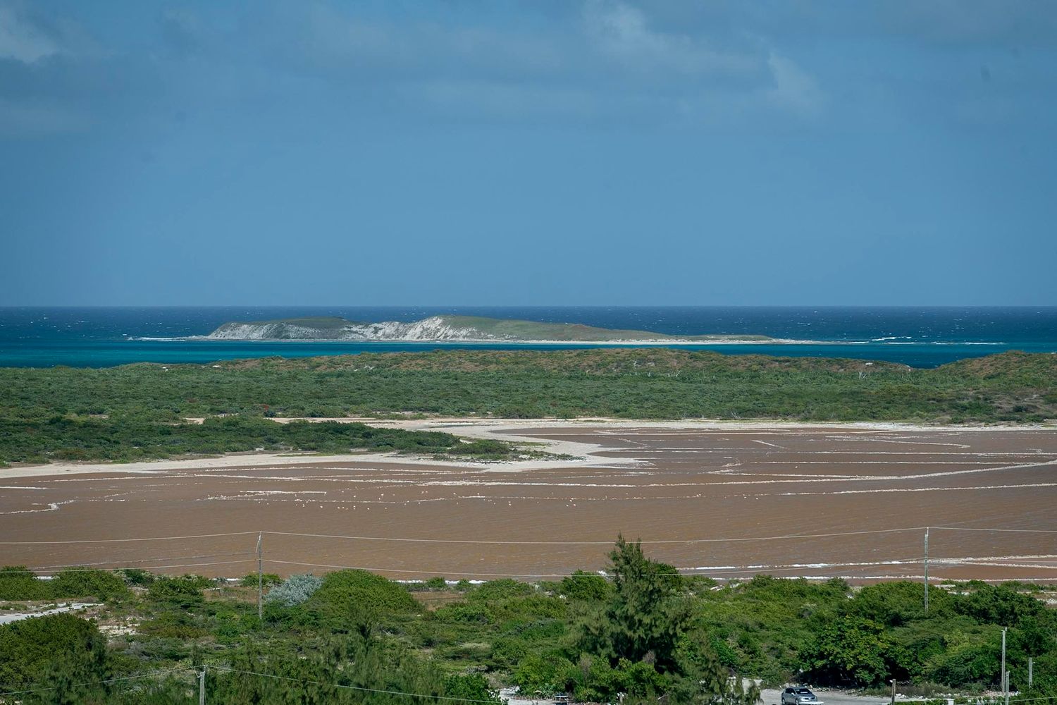 Aerial view of a sandy lagoon with turquoise ocean waters and a small island under a clear blue sky.