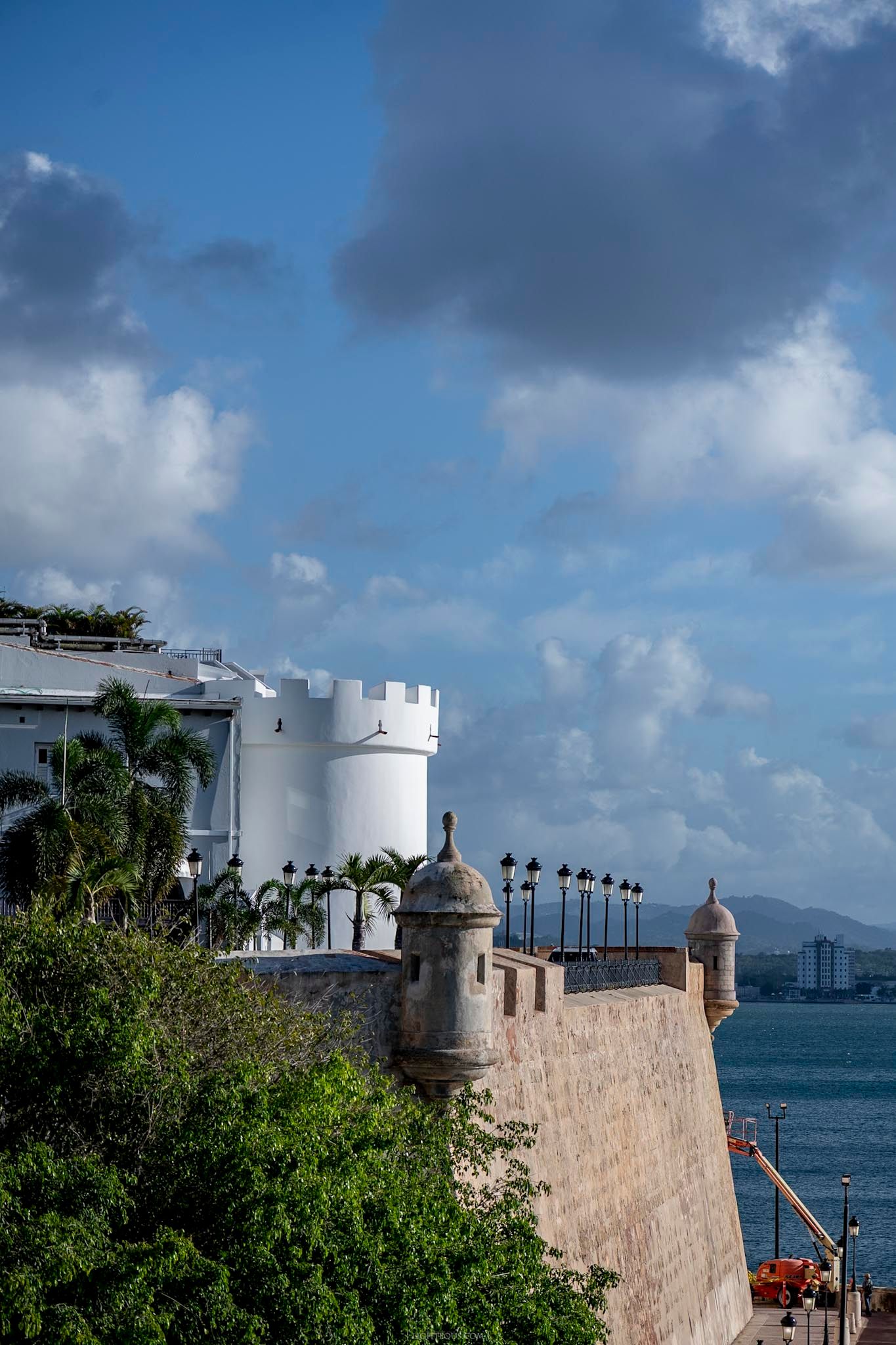 Historic white fortress walls and watchtowers of Old San Juan overlook the Caribbean Sea under a partly cloudy blue sky.