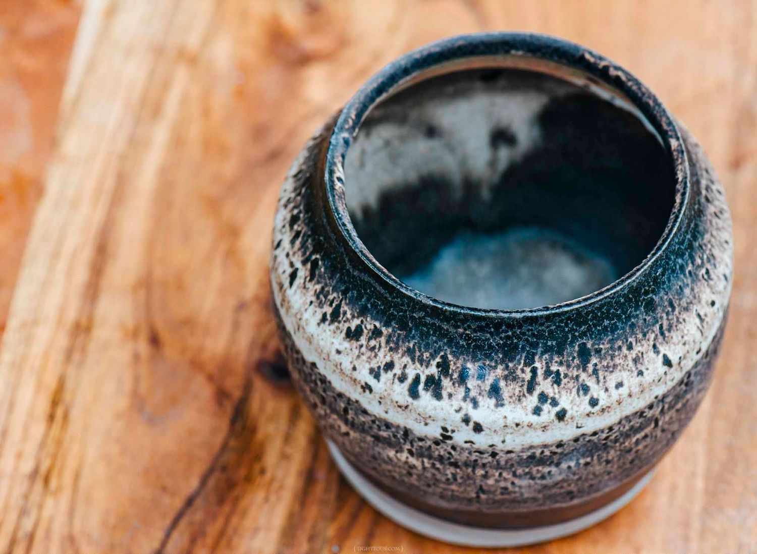 Handcrafted ceramic pottery jar with dark blue glaze interior and speckled exterior sitting on a wooden surface.