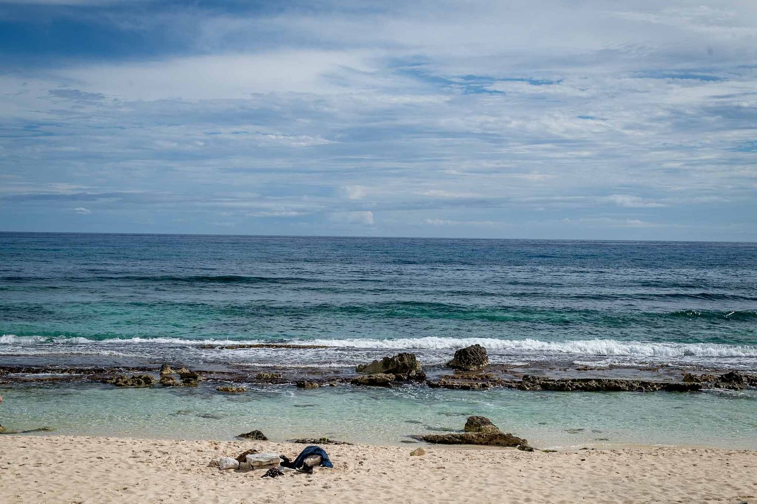 Pristine beach landscape with turquoise waters, white sand, and scattered rocks along the shoreline.