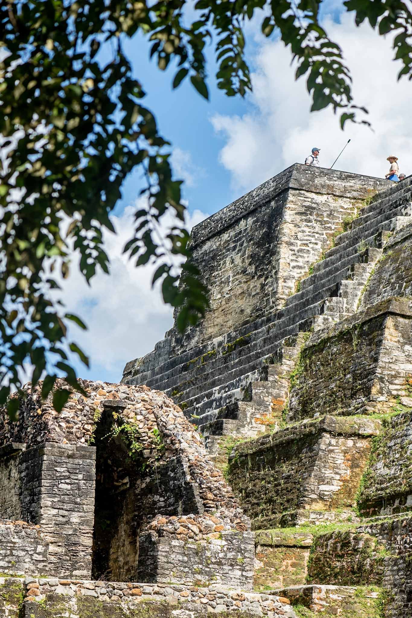 Ancient stone ruins with crumbling walls and archways against a blue sky with tree branches framing the view.
