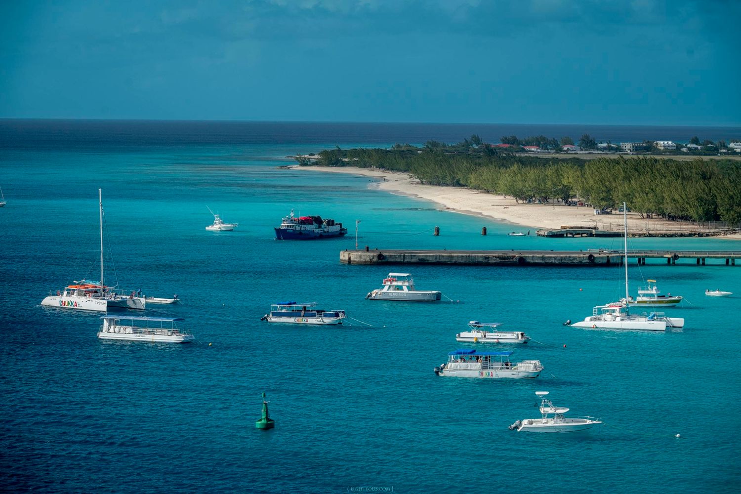 Aerial view of turquoise Caribbean waters with sailboats and motorboats anchored near a tropical island pier.