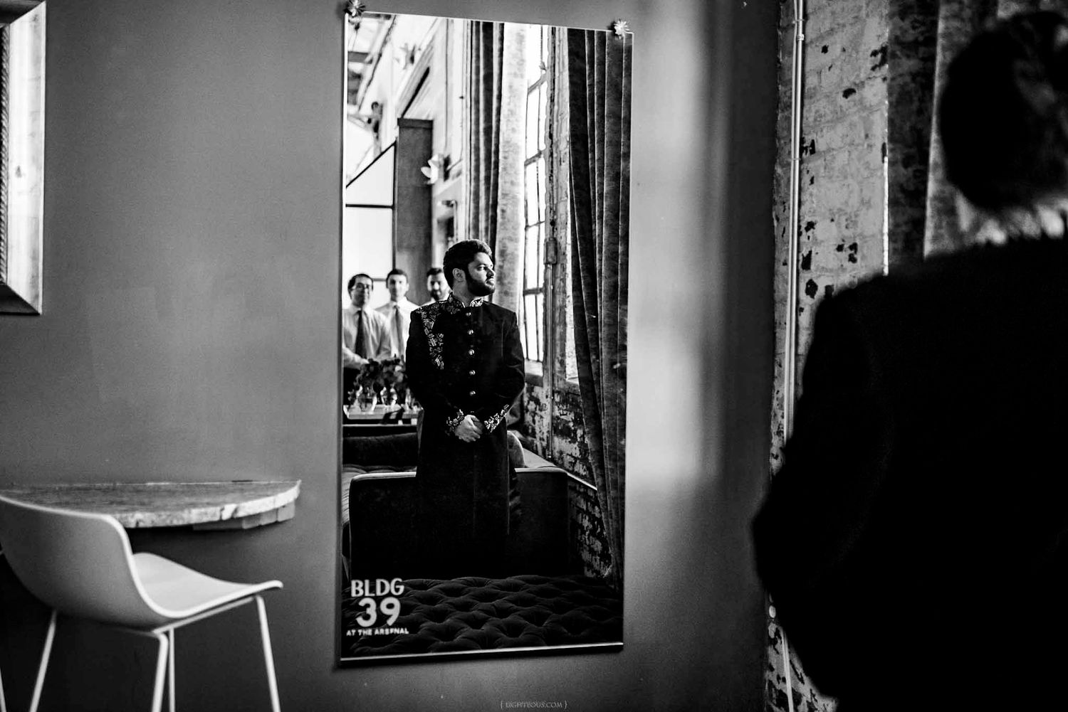 Groom in military uniform reflected in mirror at wedding venue, black and white photo.