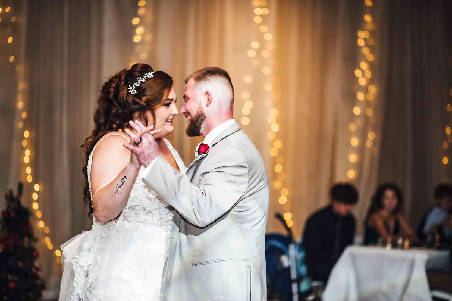 Bride and groom share their first dance, gazing into each other's eyes with warm bokeh lights in the background.