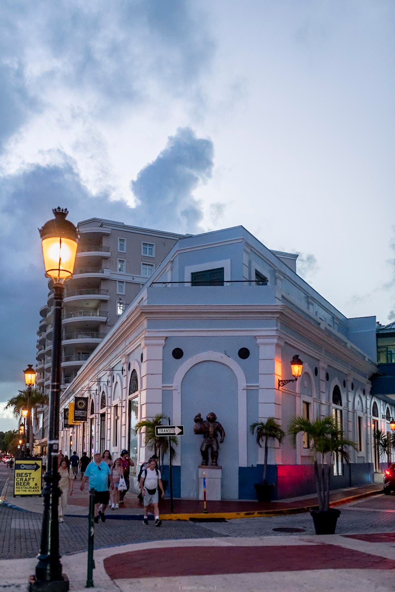 Dusk view of a white colonial building with arched windows, palm trees, and a glowing street lamp in Old San Juan, Puerto Rico.