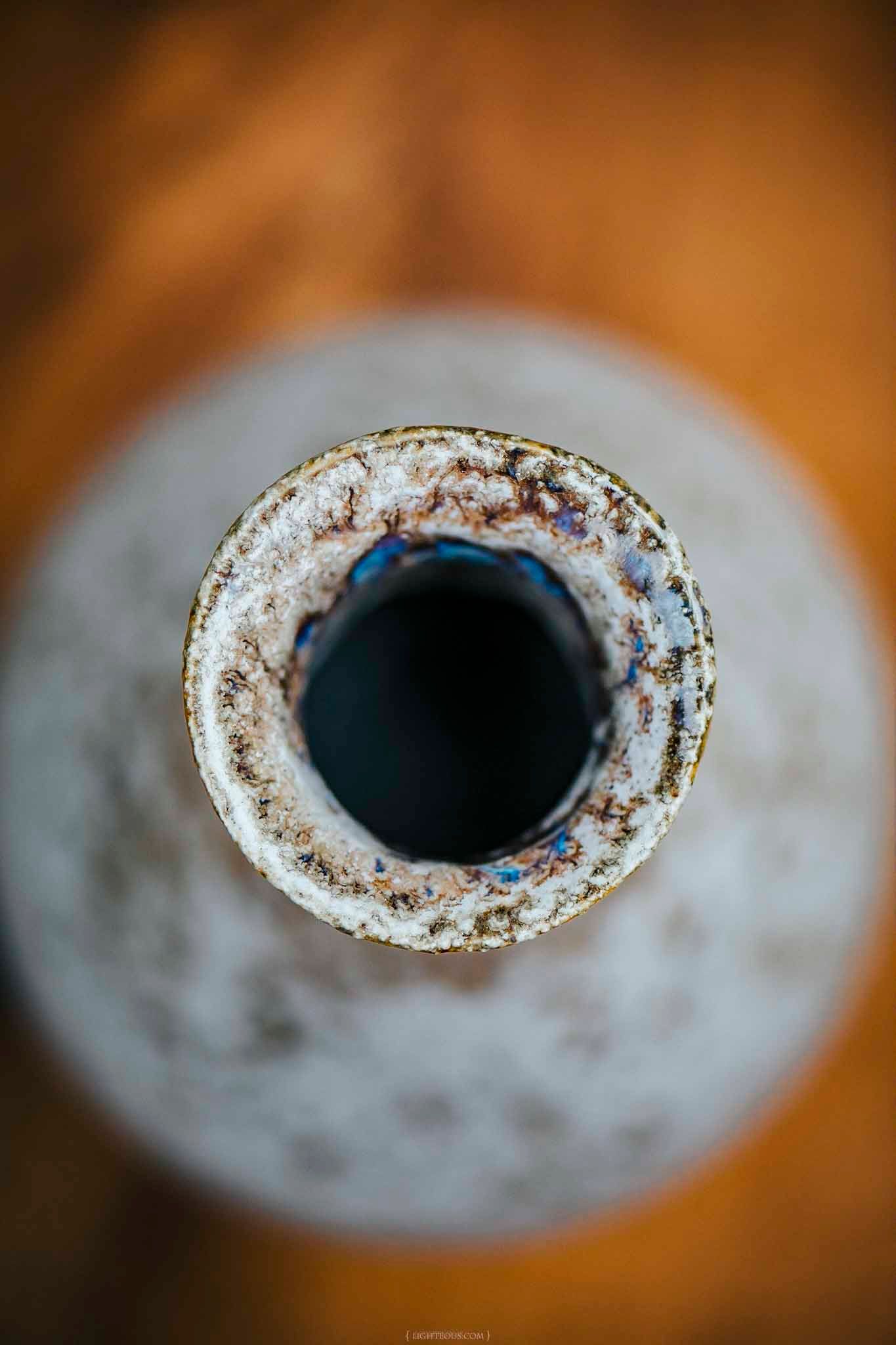 Close-up top view of a rusty, weathered metal pipe opening with white corrosion and dark interior on blurred background.