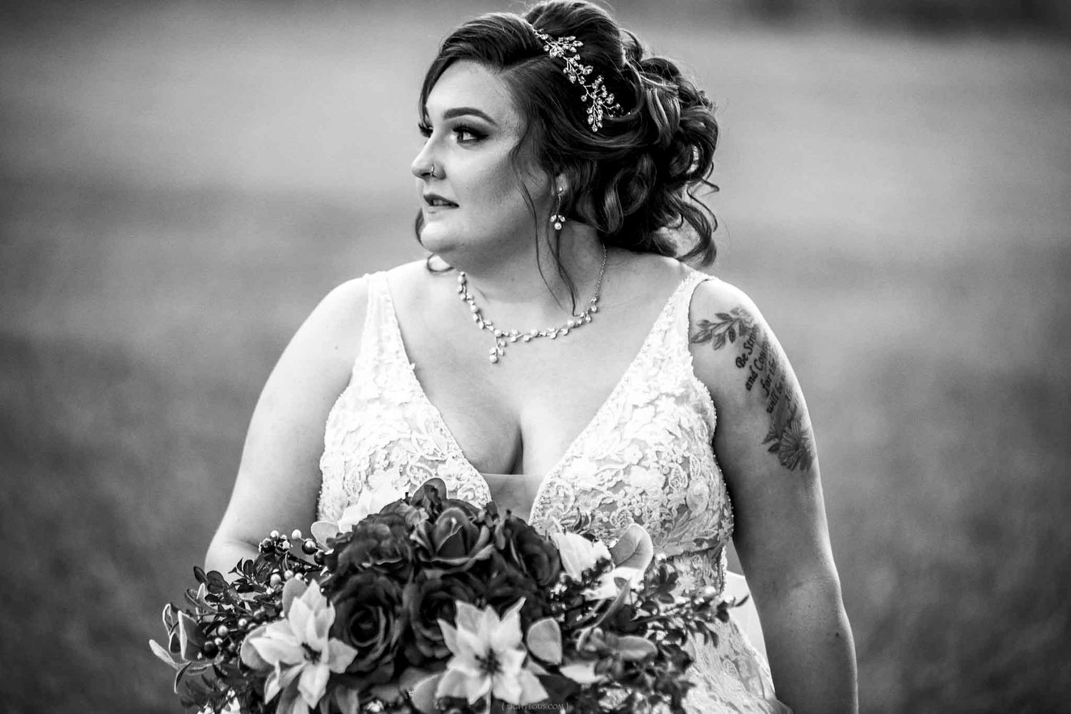Black and white bridal portrait of a woman in lace gown holding bouquet, wearing jewelry and floral hair piece.