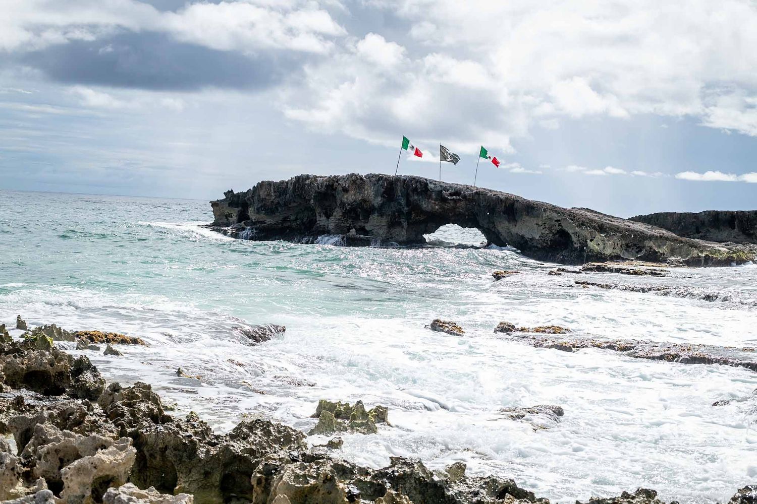 Panoramic view of a rugged coastline with white surf breaking against dark rocks under partly cloudy skies.