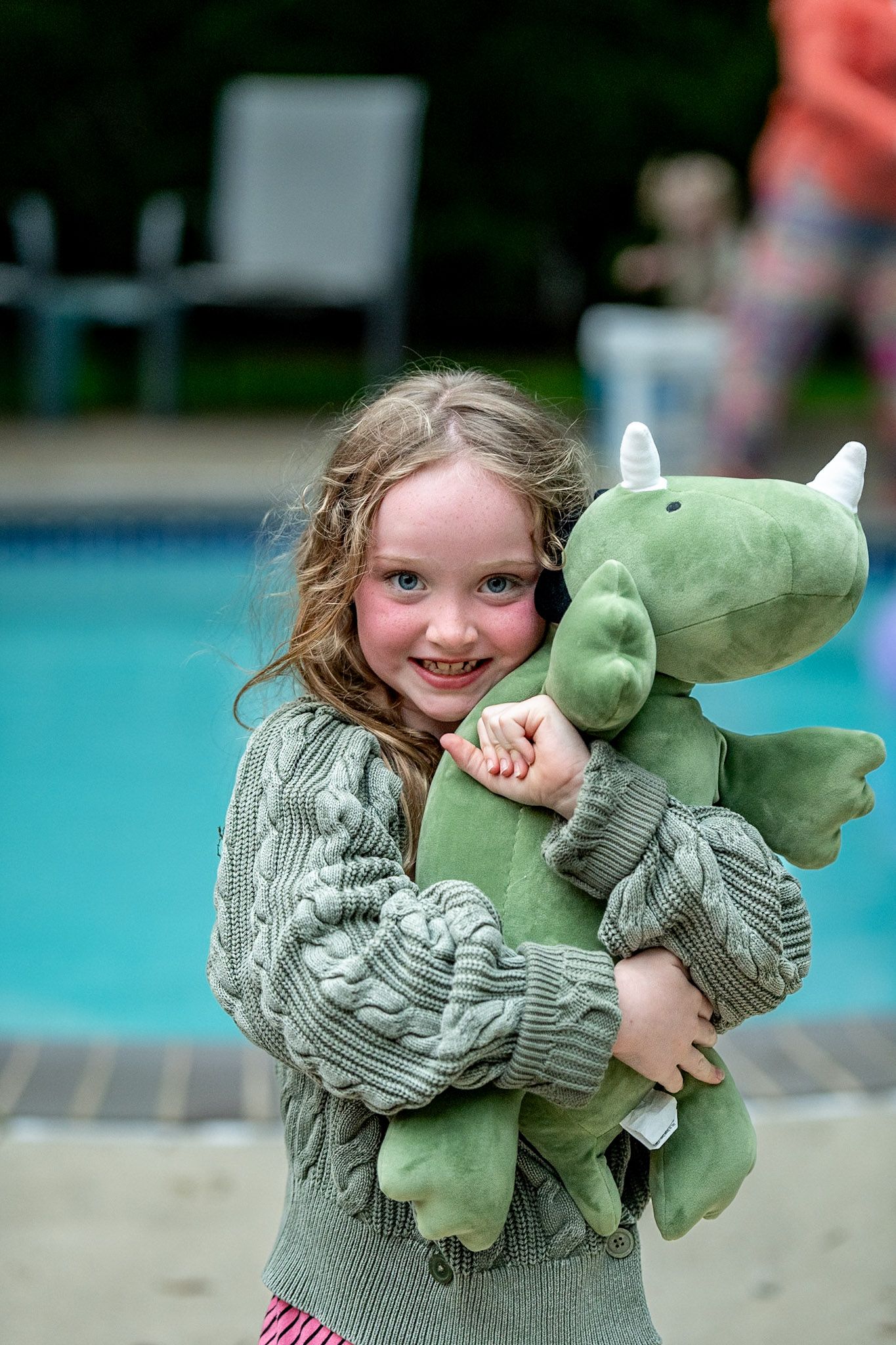Green plush dragon toy being held against pool background.
