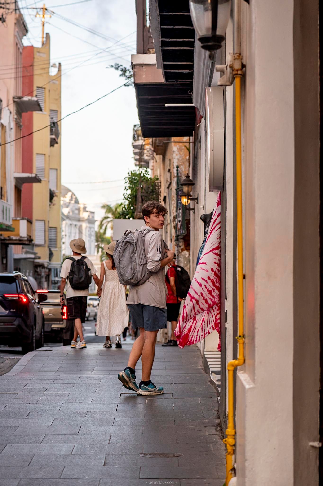 A tourist with a backpack explores a colorful narrow street in Old San Juan, Puerto Rico.