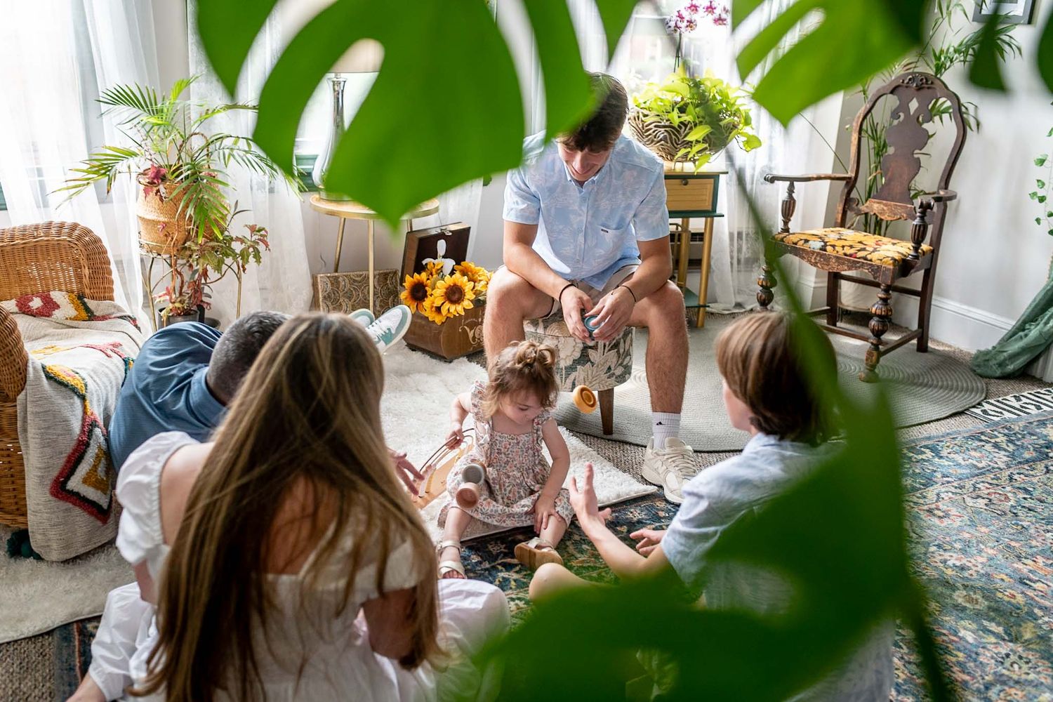 Candid family moments photographed in a bright room with lush green plants.