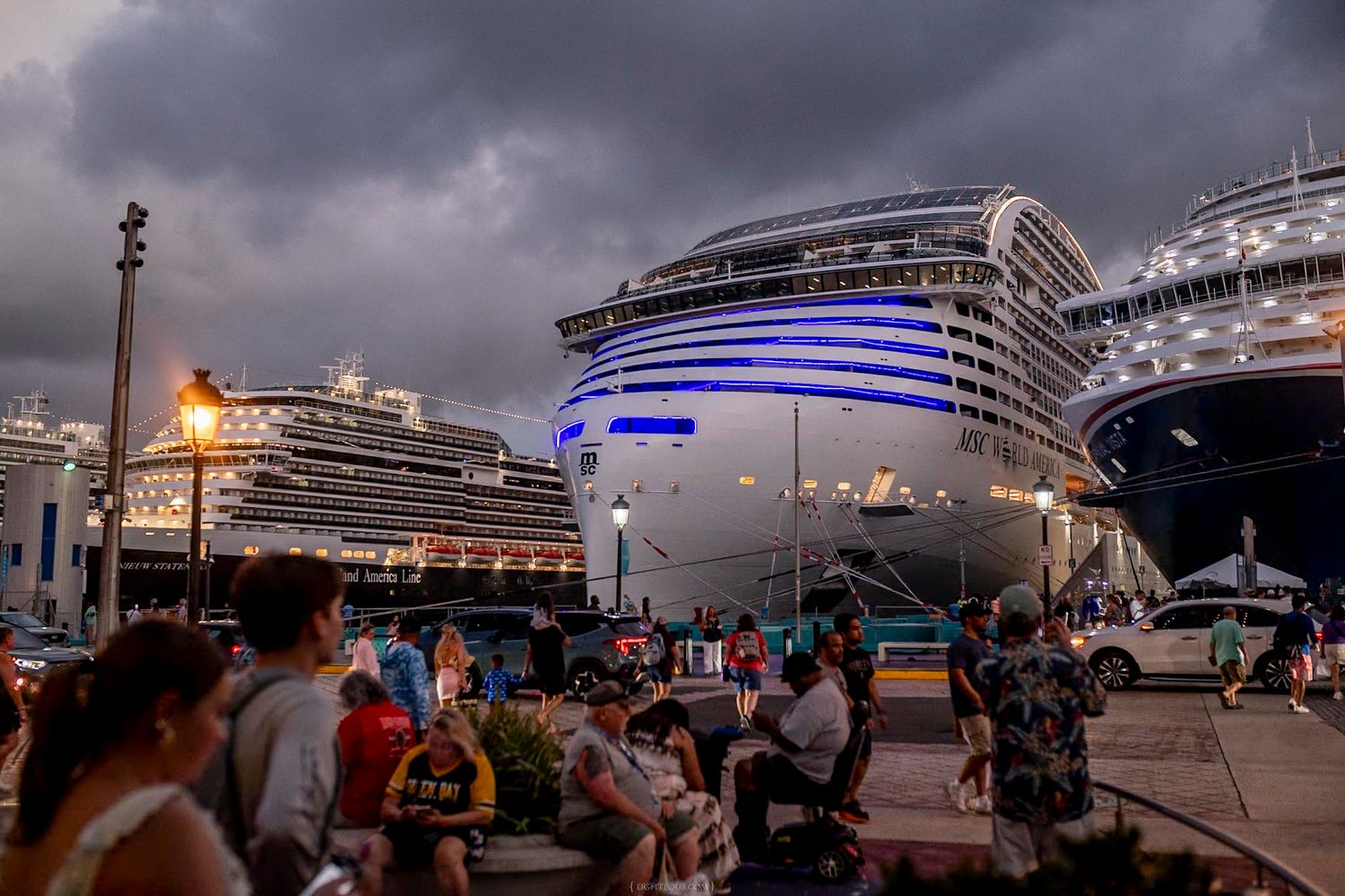 Large cruise ships docked at a busy port under dramatic cloudy skies at dusk.
