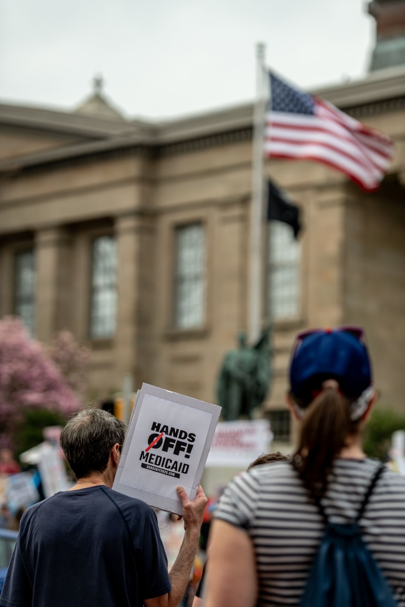 Demonstrators hold signs about Medicaid with American flags and government building visible in background.