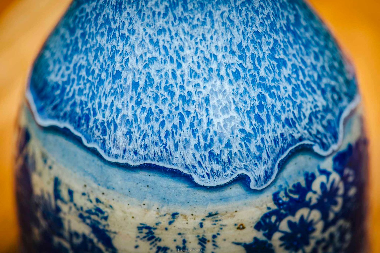 Close-up of a blue and white glazed ceramic vase with textured crystalline glaze on wooden surface.