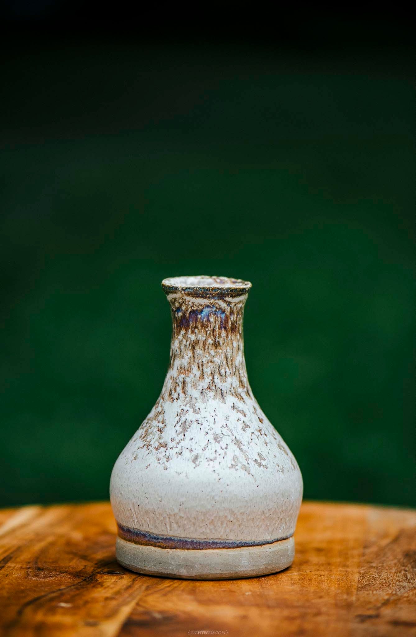 Rustic white and brown glazed ceramic vase on a wooden surface with green background.