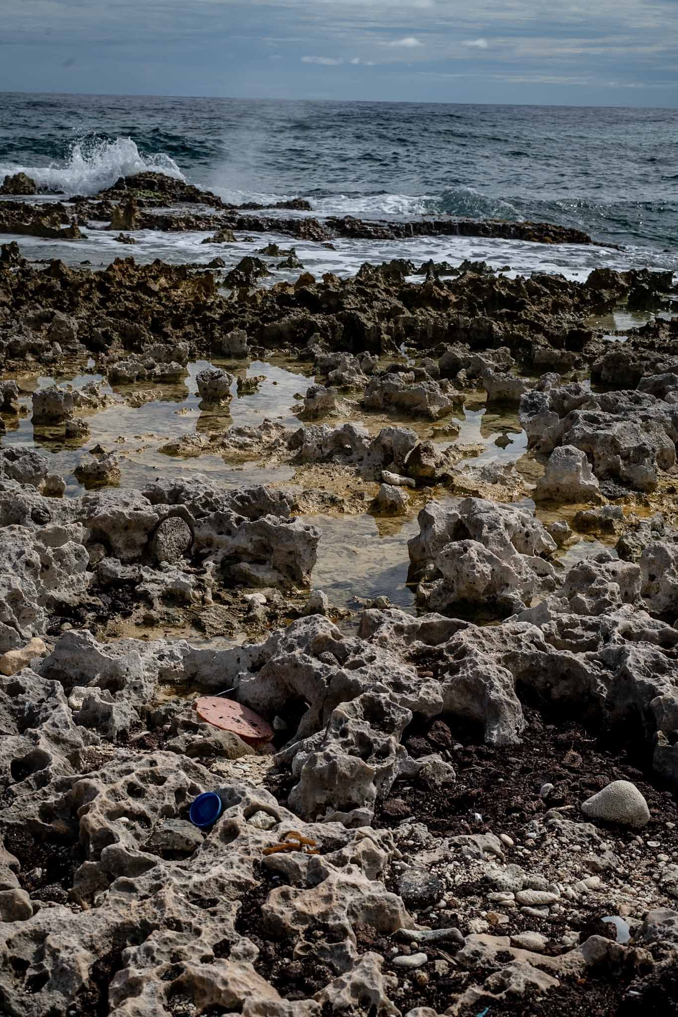 Rocky volcanic coastline with waves crashing against jagged formations under an overcast sky.