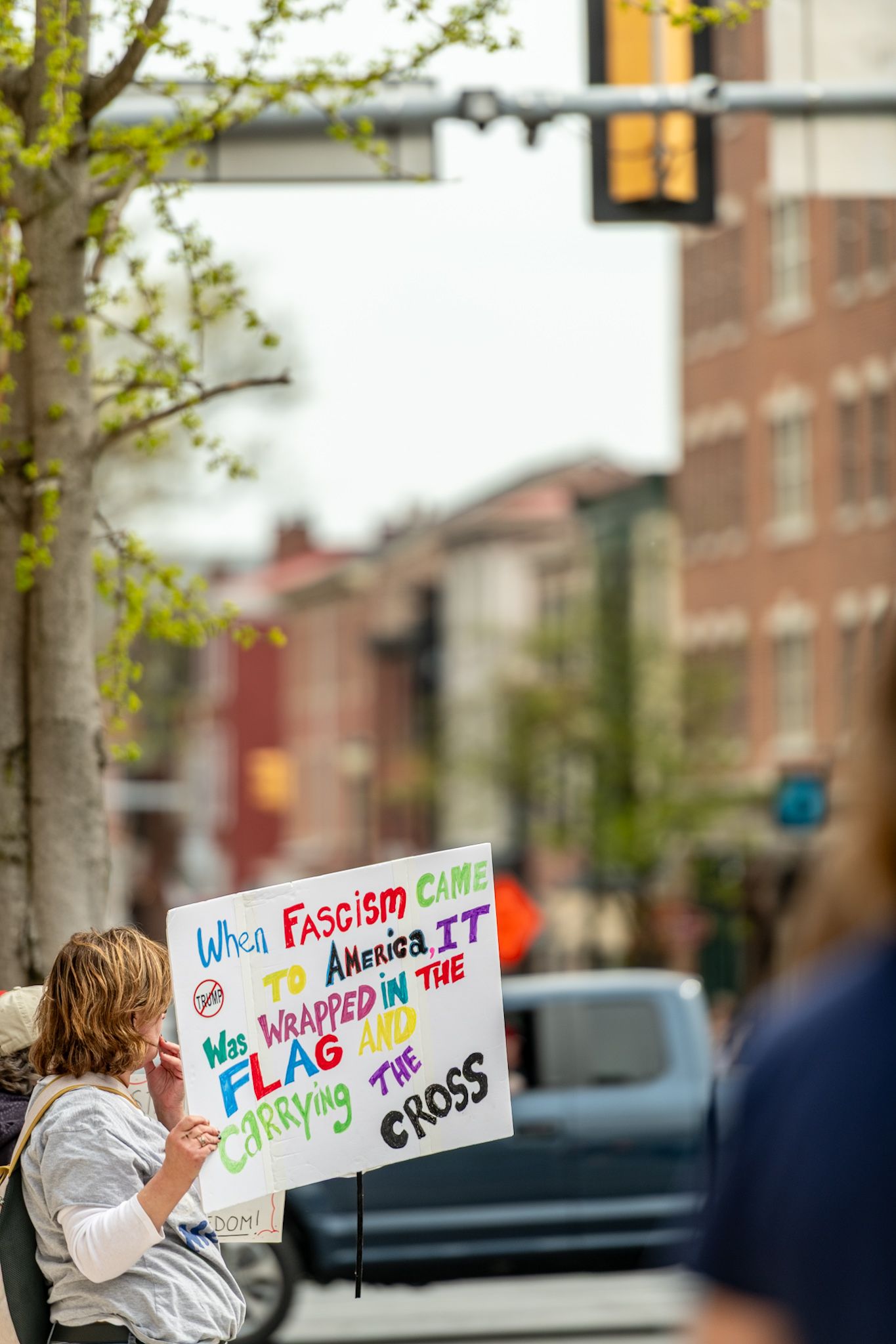 Protest signs visible along a tree-lined urban street during a political demonstration.